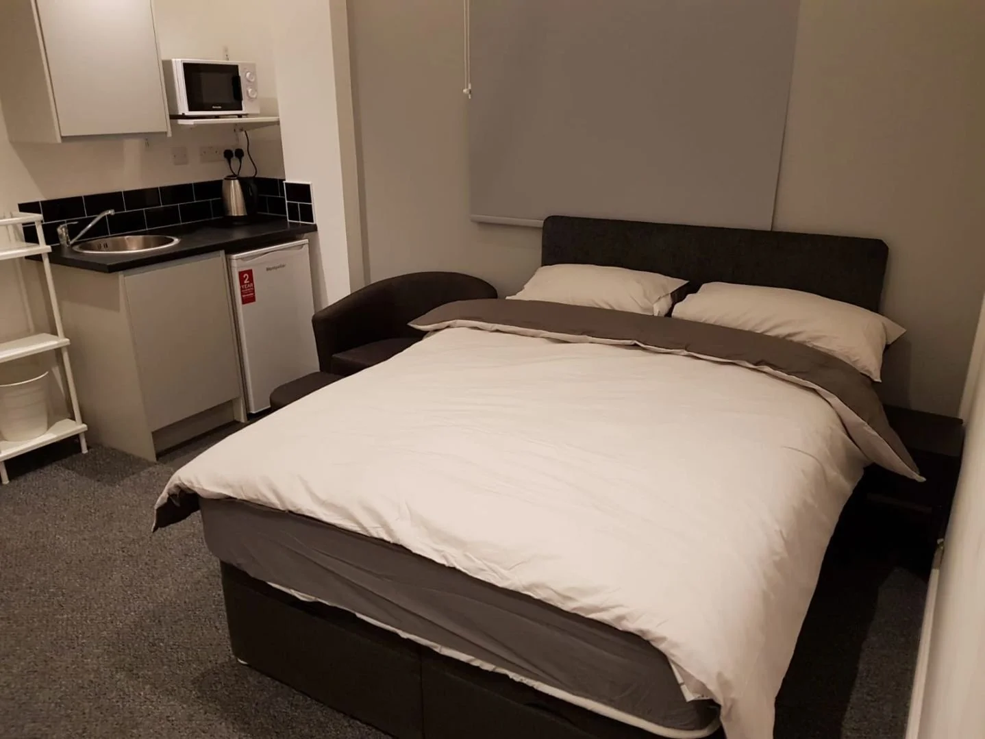 A compact hotel room with a bed, small kitchenette, and sitting area.