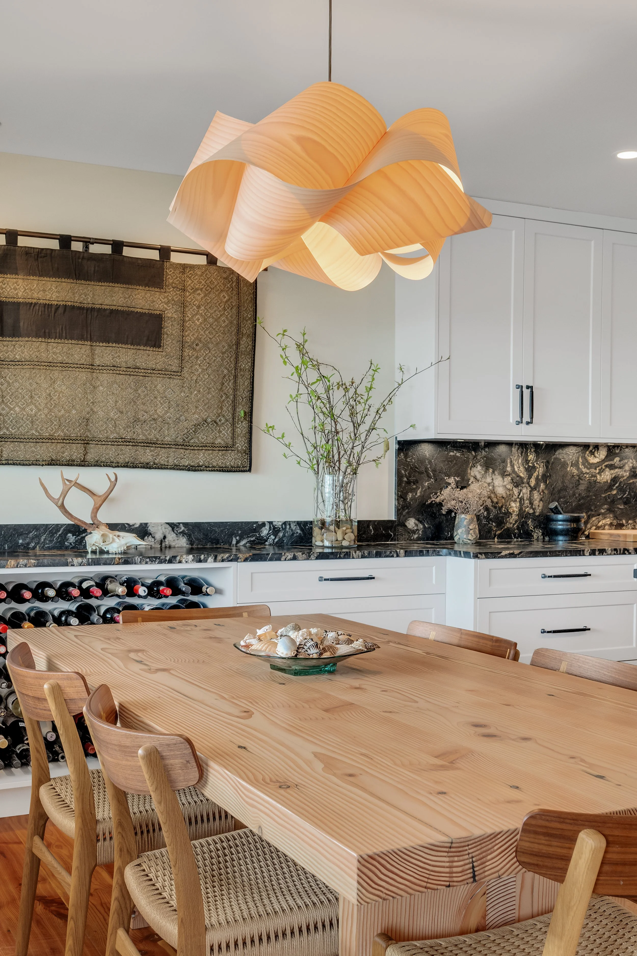Modern kitchen with a wooden dining table, a wine rack, and a decorative chandelier overhead.