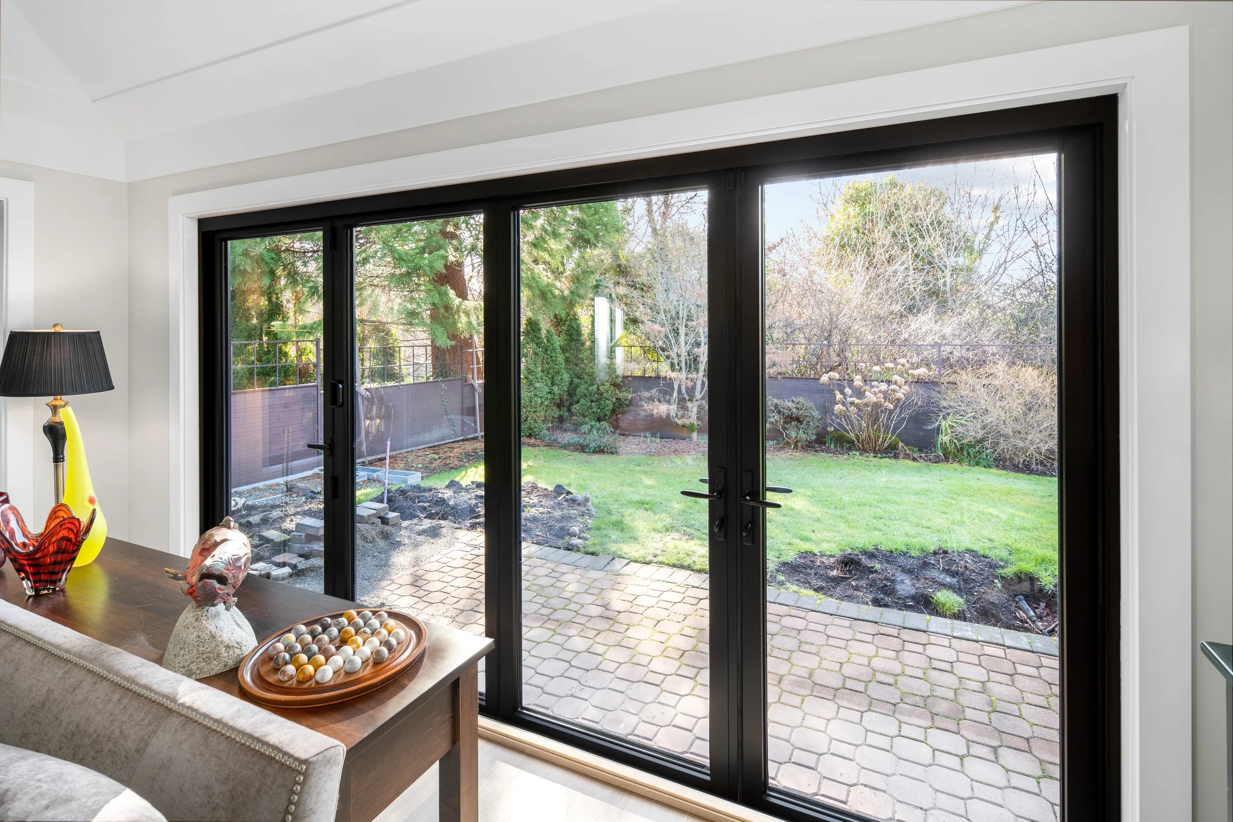 Interior view of a sliding glass door leading to a backyard with grass, trees, and a brick patio.
