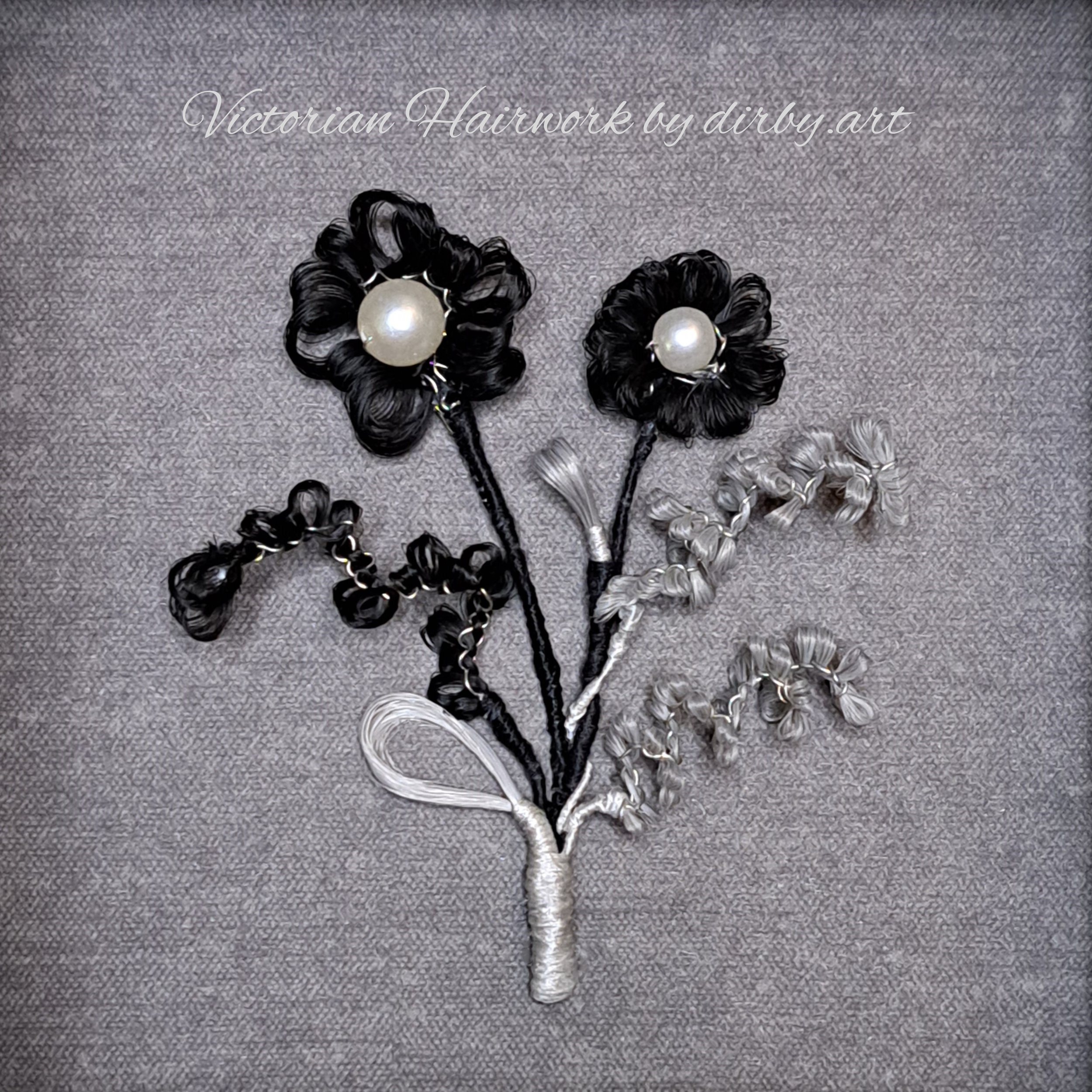 A Victorian-style hairwork posy bouquet, made of black, grey, and white human hair, placed on a grey background, created by historian and artist Diane Irby.