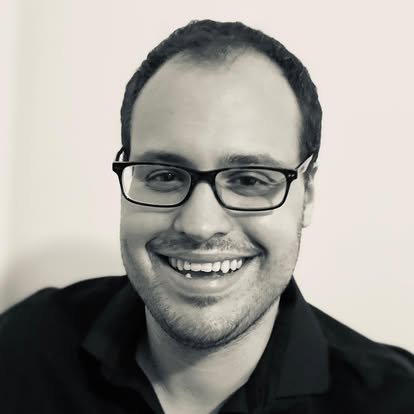 Black and white photo of a smiling man wearing glasses and a dark shirt.
