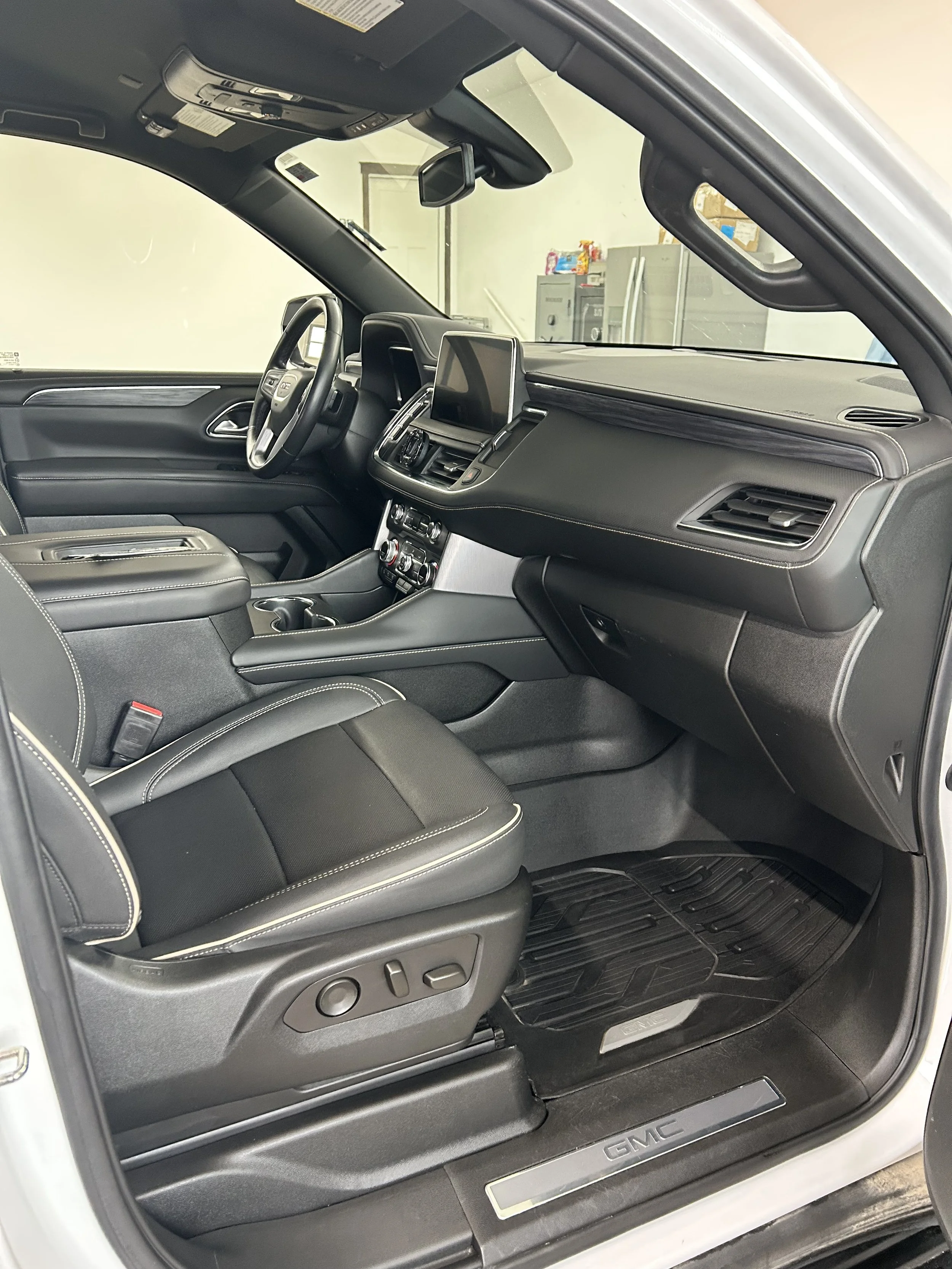The interior of a GMC vehicle showing the driver's seat, dashboard, steering wheel, center console, and front passenger seat with black upholstery and modern controls.