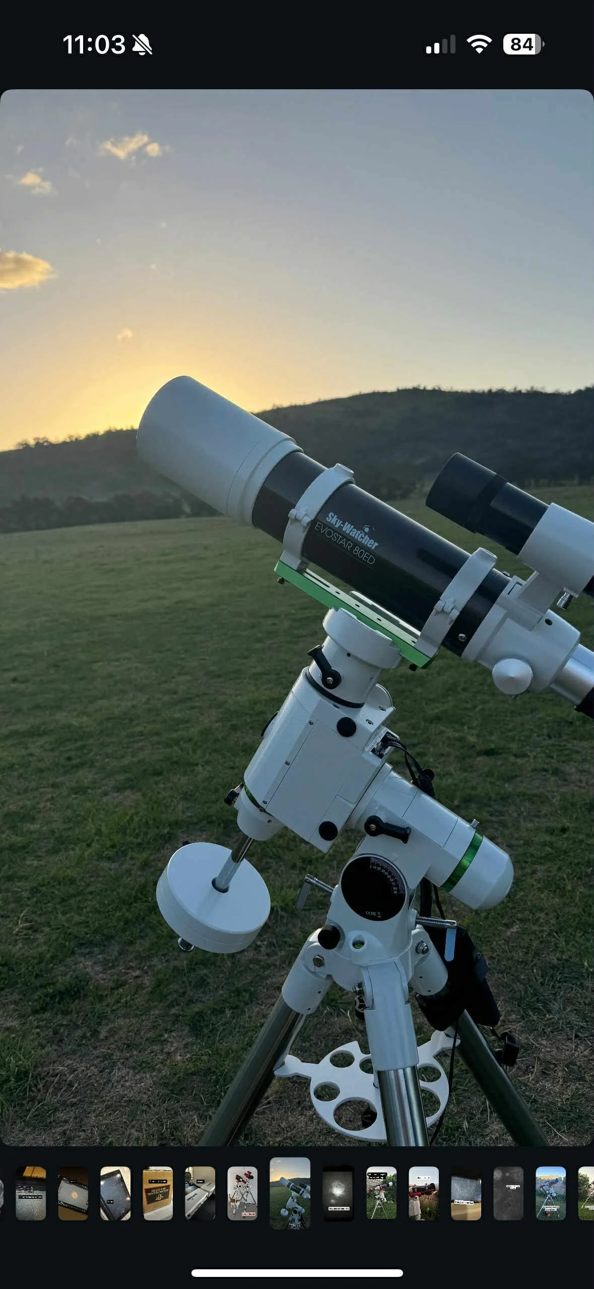 A telescope set up outdoors on a grassy field with hills in the background during sunset.