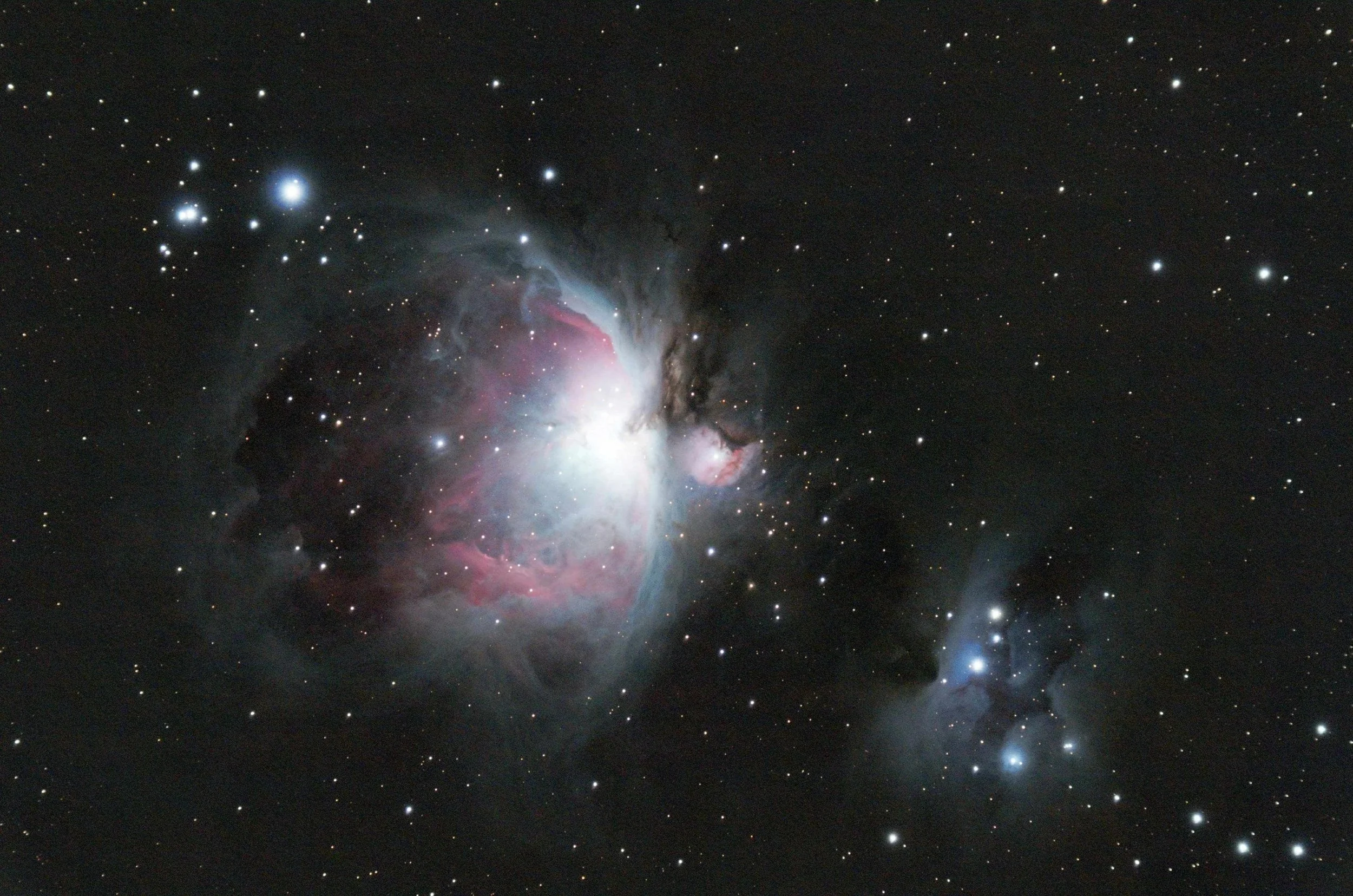 A detailed image of a nebula in space with bright stars and colorful gas clouds, mainly pink, white, and smoky gray, against a black starry background.