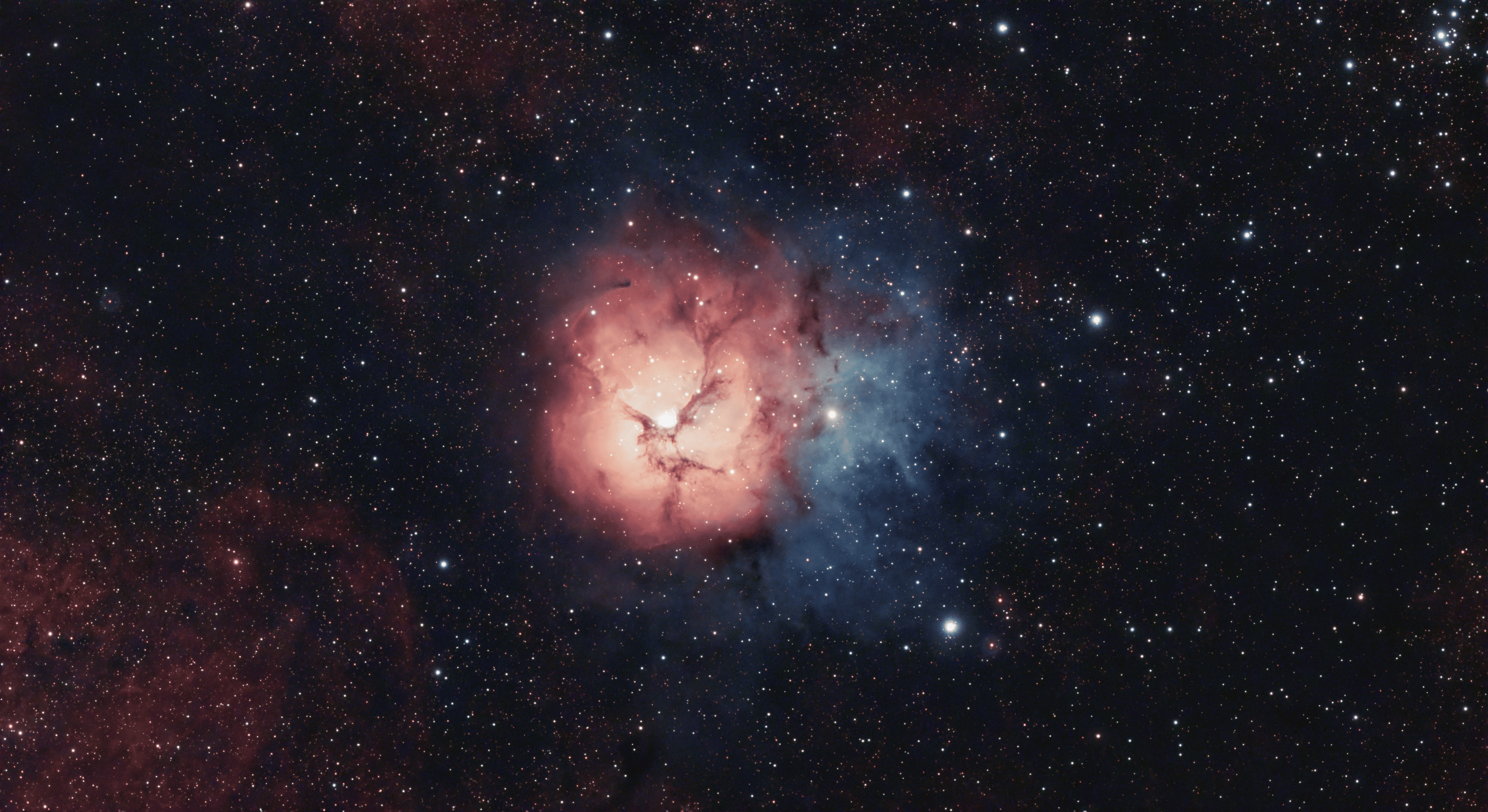A colorful image of space showing a nebula with pink, blue, and black regions, surrounded by numerous stars.