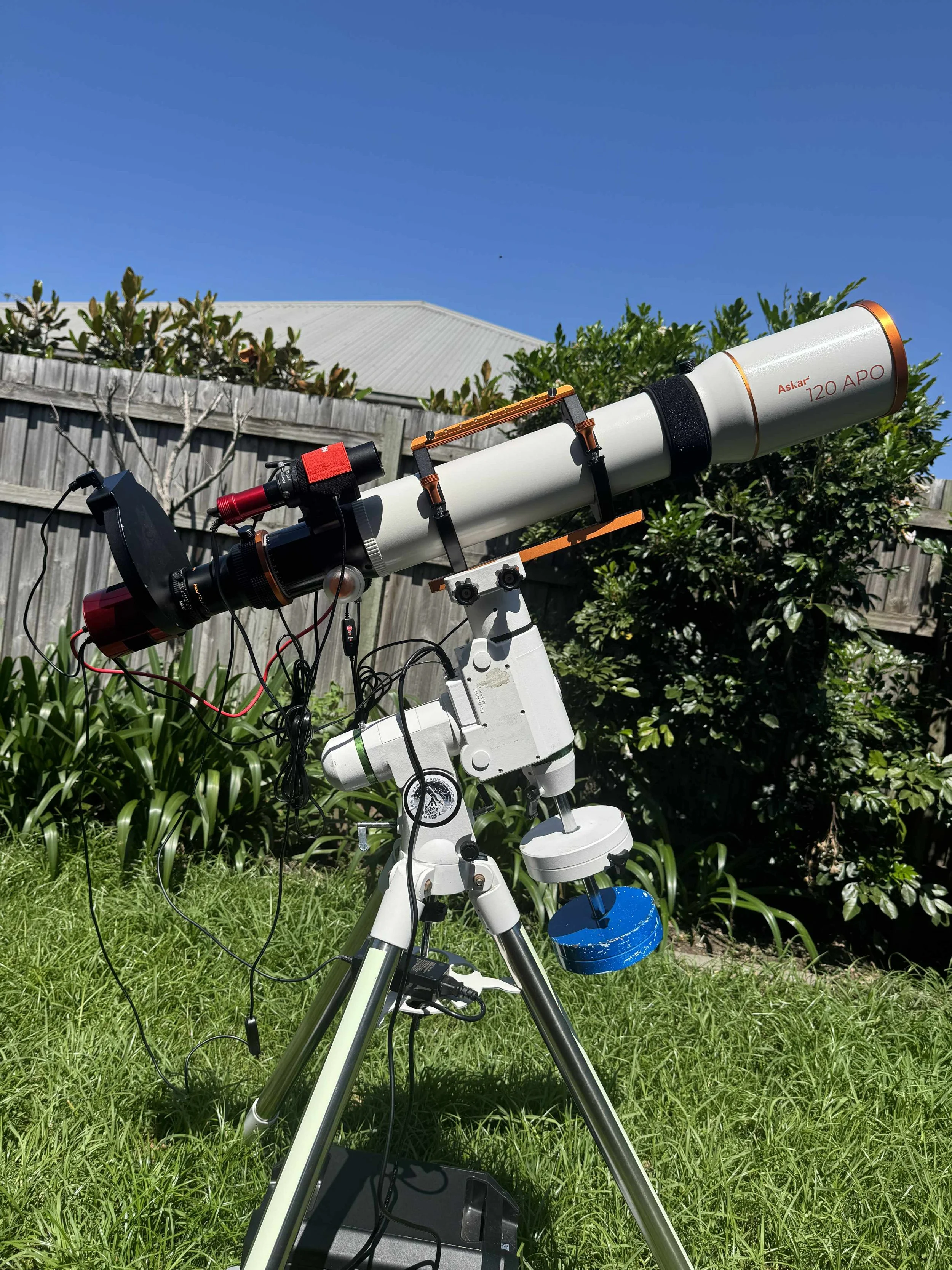 A telescope set up outdoors on a grassy area at night, pointing toward the sky, with a wooden fence and trees in the background.