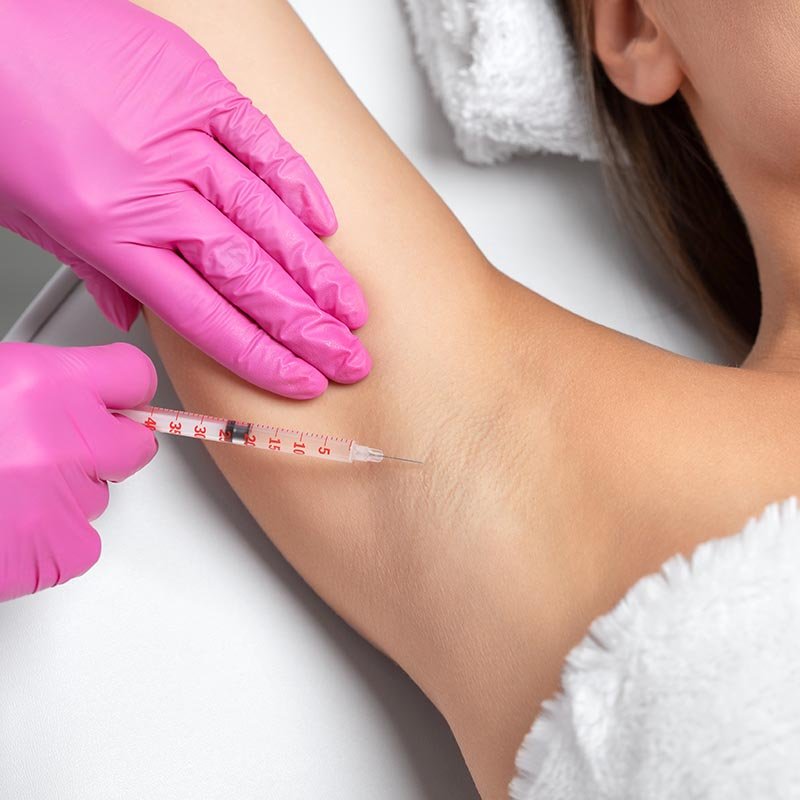A healthcare professional wearing pink gloves administering an injection in a person's armpit, likely for medical testing or treatment.