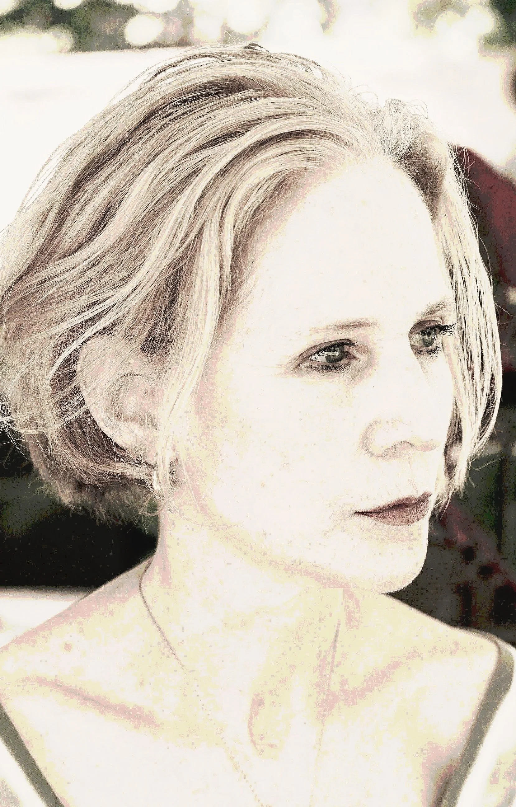 Close-up portrait of a woman with short, blonde, wavy hair, light skin, blue eyes, and red lipstick, with a soft focused background.