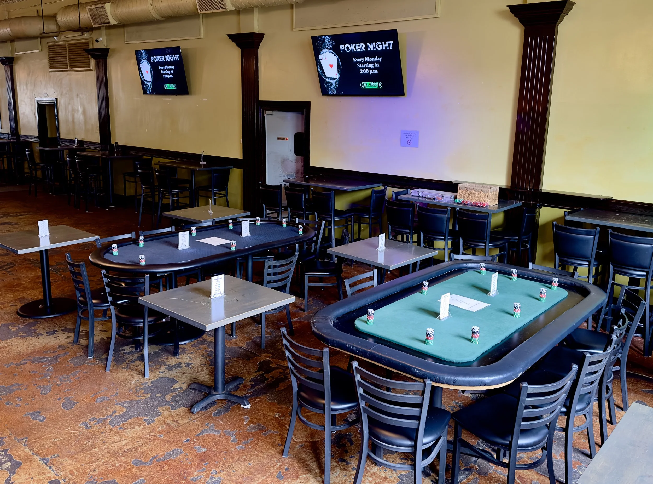 Empty poker room with poker tables, chairs, and screens announcing poker night every Monday at 7:00 p.m.