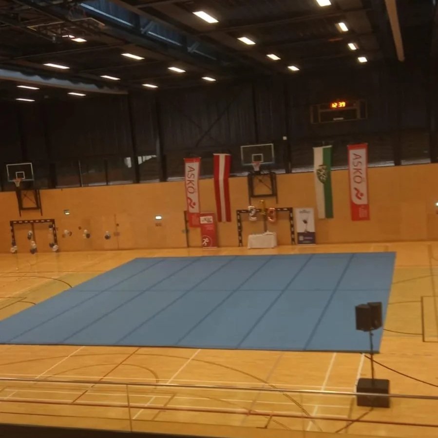 Leerer Sporthalle mit blauner Bodenfläche und Flaggen an der Wand.
