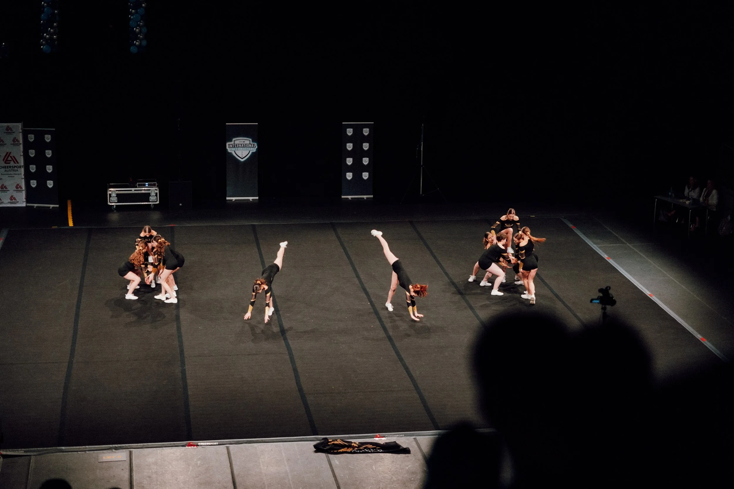 Sportlerinnen führen eine Cheerleading-Performance auf einer Turnmatte bei einem Wettbewerb auf.