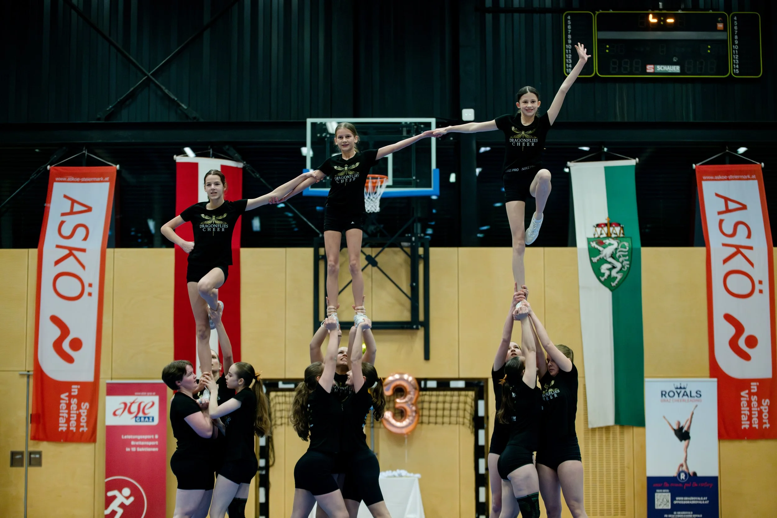 Drei junge Mädchen führen im Turnverein eine akrobatische Balancierübung mit Menschen auf.