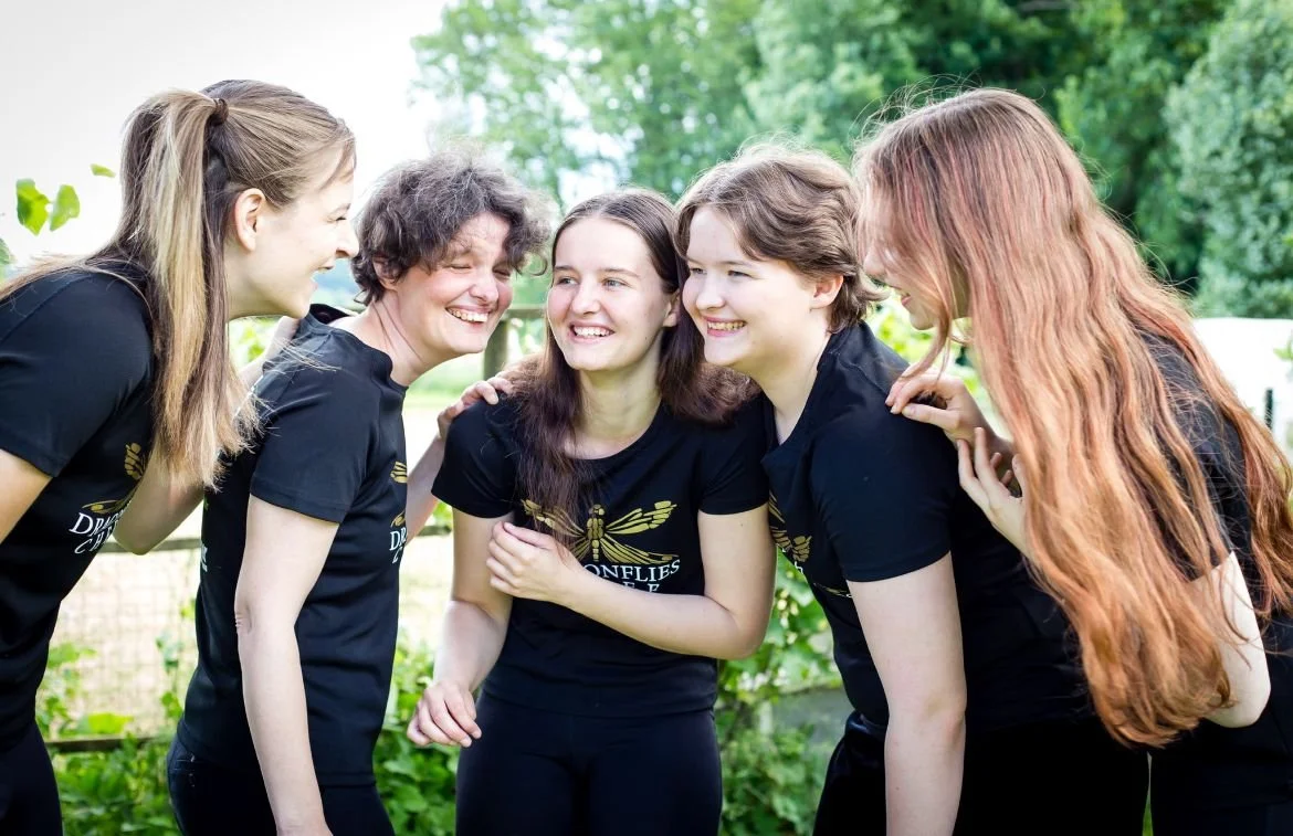 Fünf junge Frauen lachen und umarmen sich im Freien.