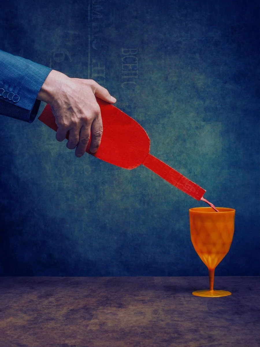 A person pouring red liquid from a large red bottle into an orange glass.