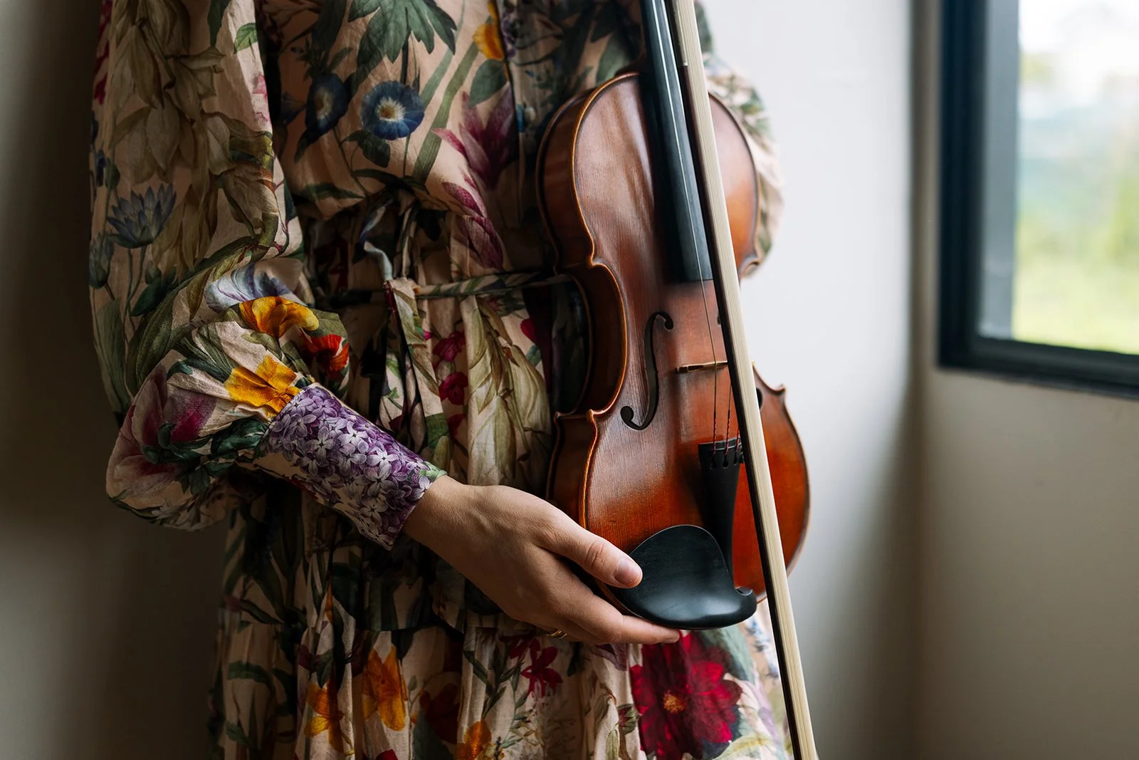 Tabea Sitte-Irwin in a floral dress holding a violin and bow by a window