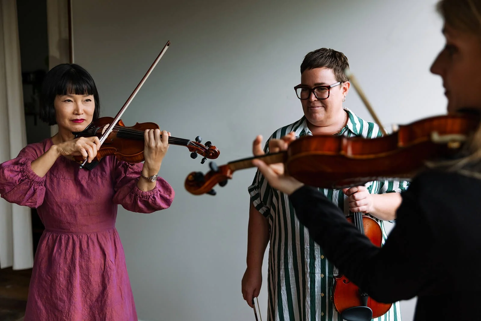 Three women playing violins together in a room.
