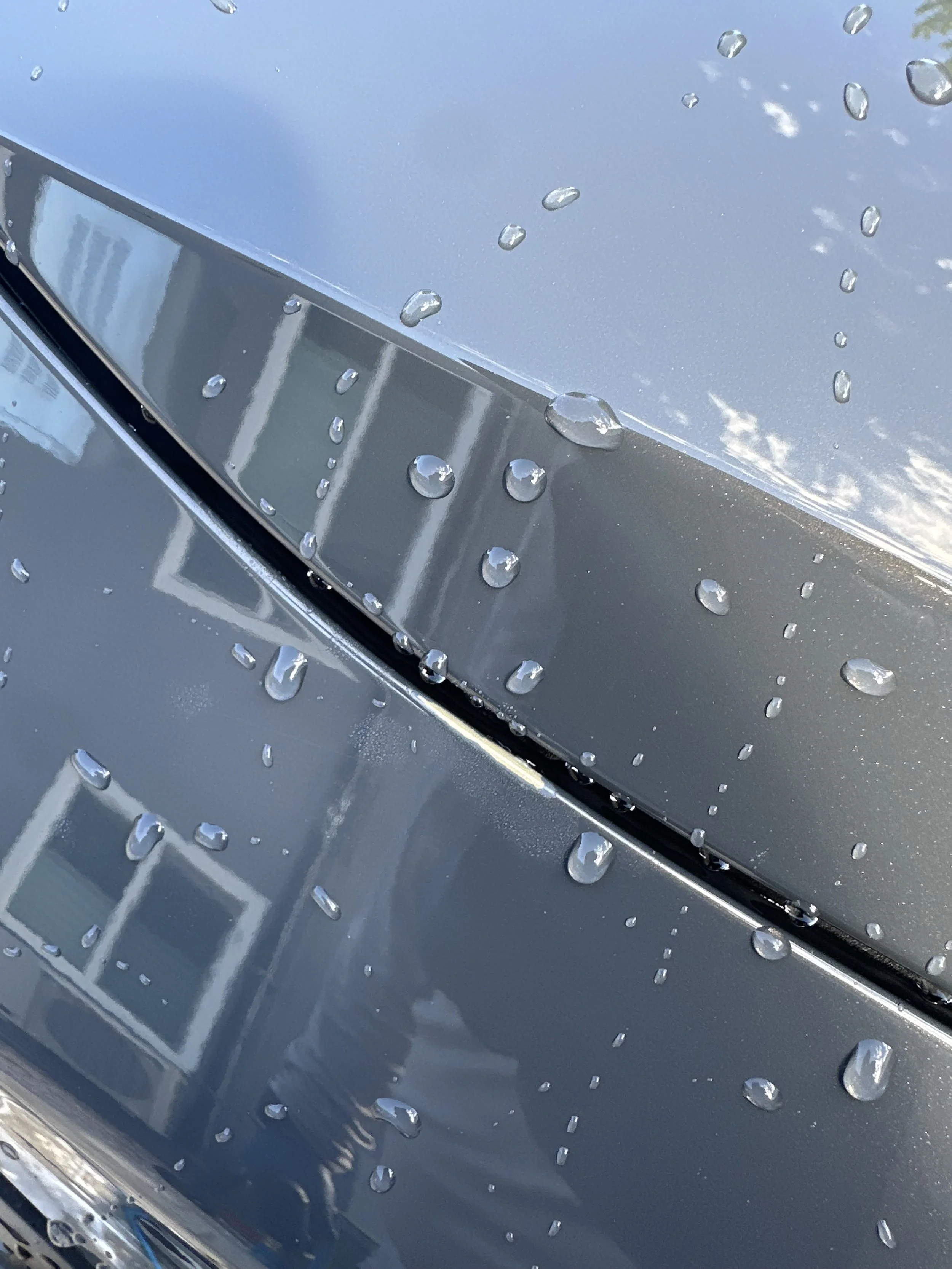 Close-up of a metallic surface with water droplets on it, possibly the hood of a car.