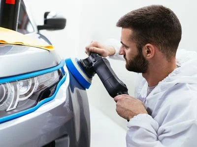 Man using a polishing machine on a car's headlight
