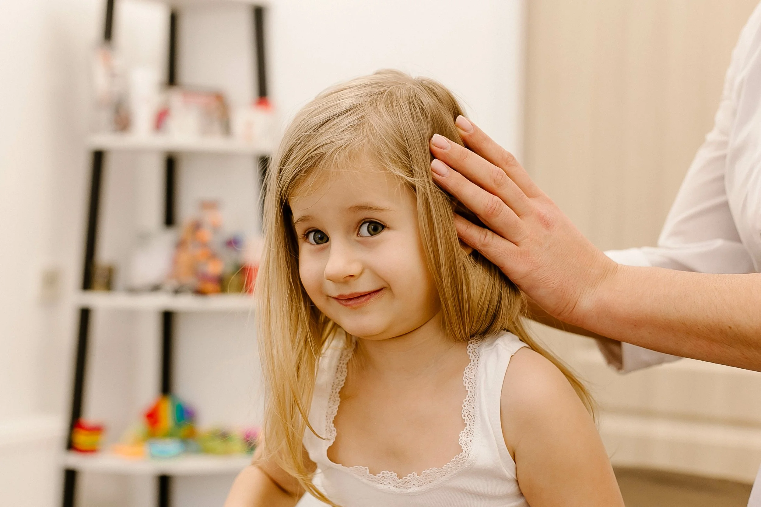 Young girl receiving craniosacral therapy, smiling as a practitioner gently places hands on her head in a calm, child-friendly setting.
