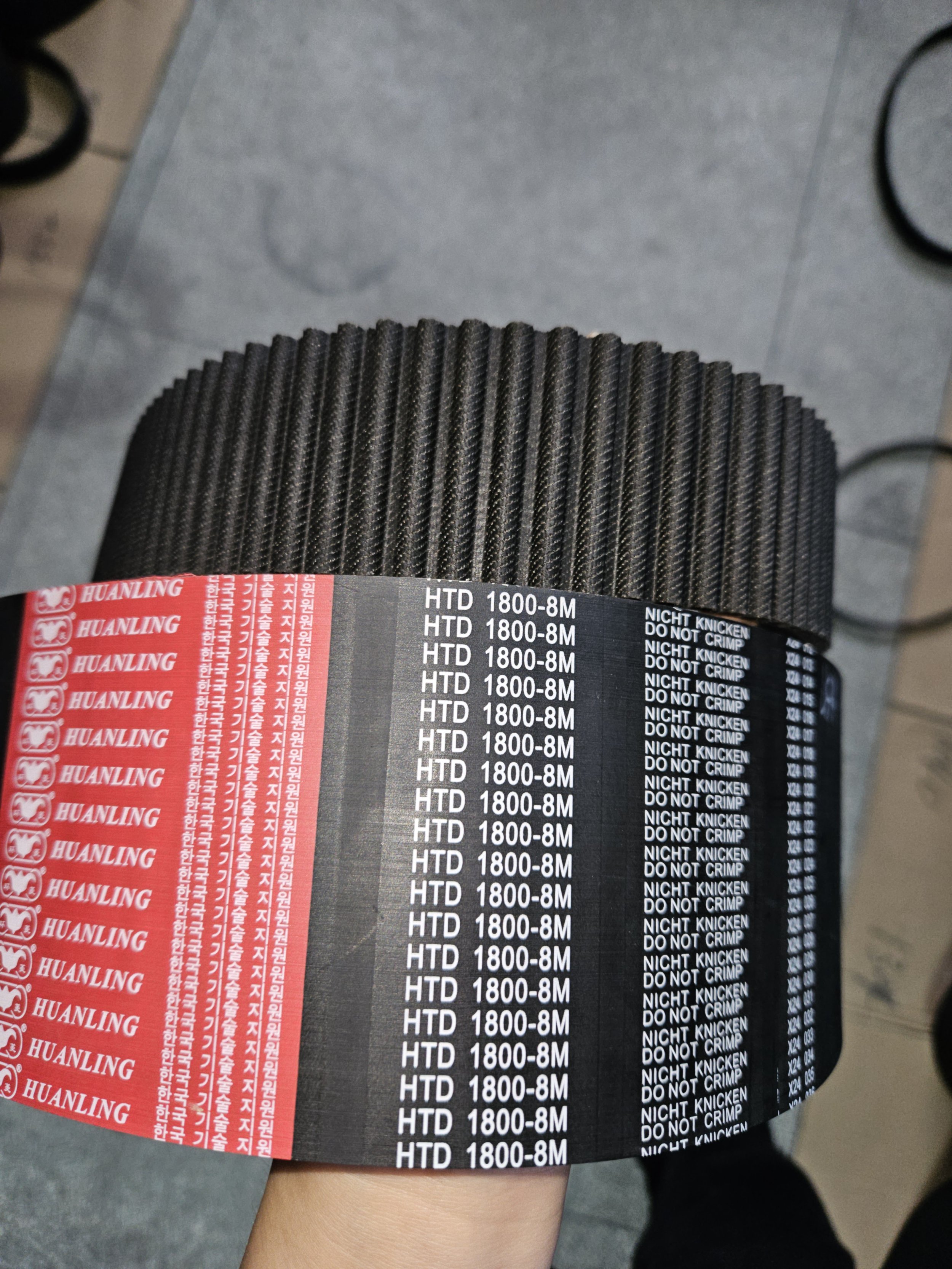 A person holding a roll of black automotive high-performance air filters with red and black labels, featuring text including 'HUANLING,' 'HTD 1800-8M,' and 'NIGHT KNICKEN DO NOT CRIMP'.