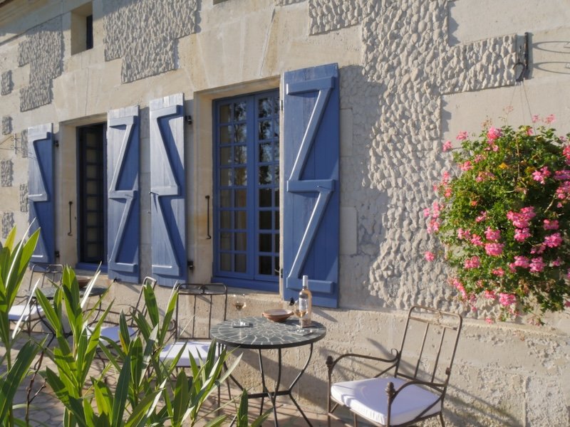 Blaue Fensterläden an einem Landhaus, davor ein Tisch auf der Terrasse