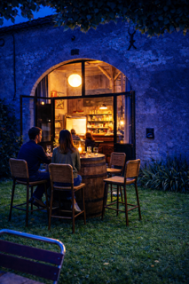 Pop-up-Restaurant vor historischem Steingebäude in Frankreich bei Abendlicht, Tische mit Gästen und Beleuchtung