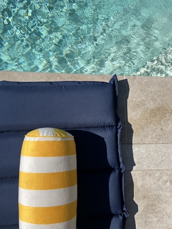 Blaue Poolauflage mit gelb-weiß gestreifter Rolle und Wasser im Hintergrund