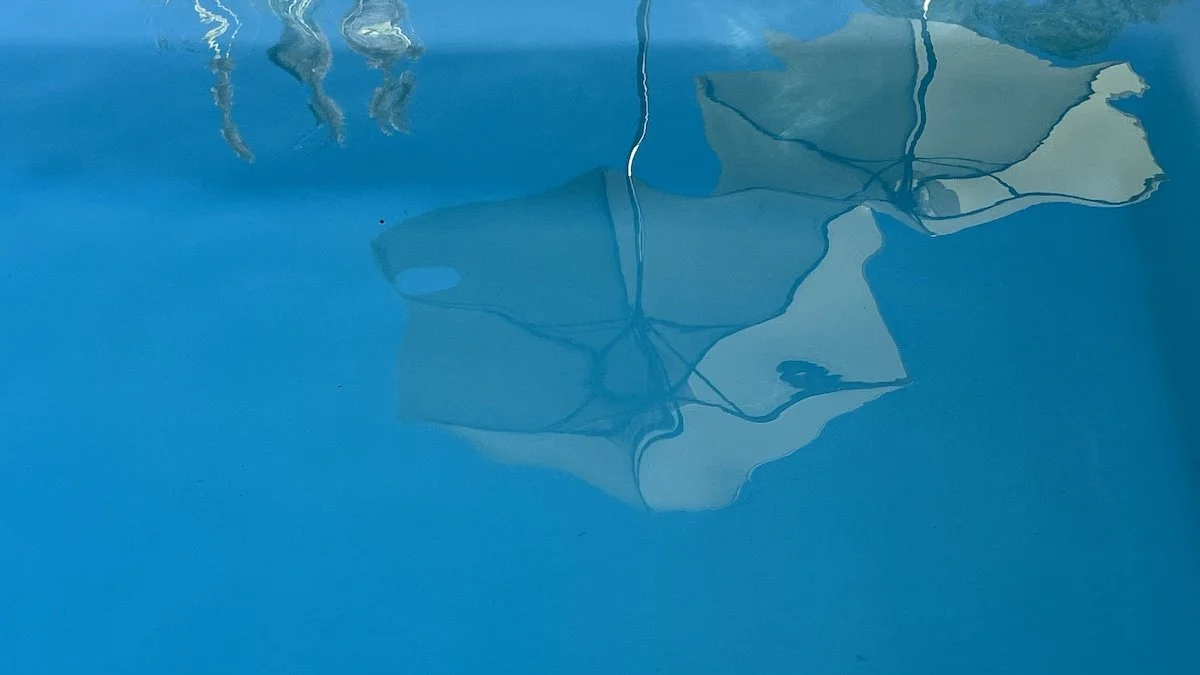 Spiegelung von Sitzbereich, Pool und Sonnenschirm im Wasser