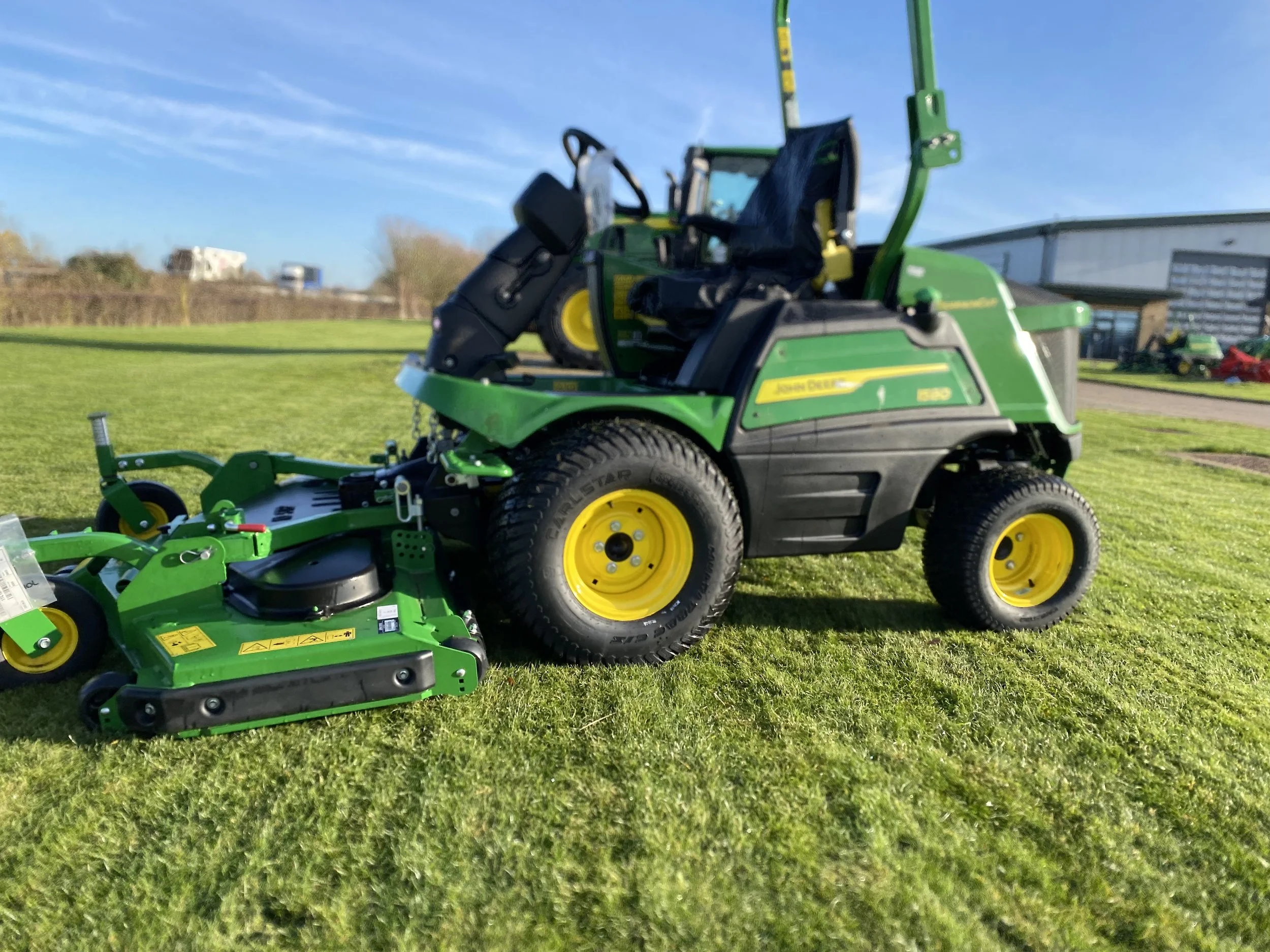 A green and yellow John Deere tractor with an attached mower deck on a grassy field, clear blue sky in the background.