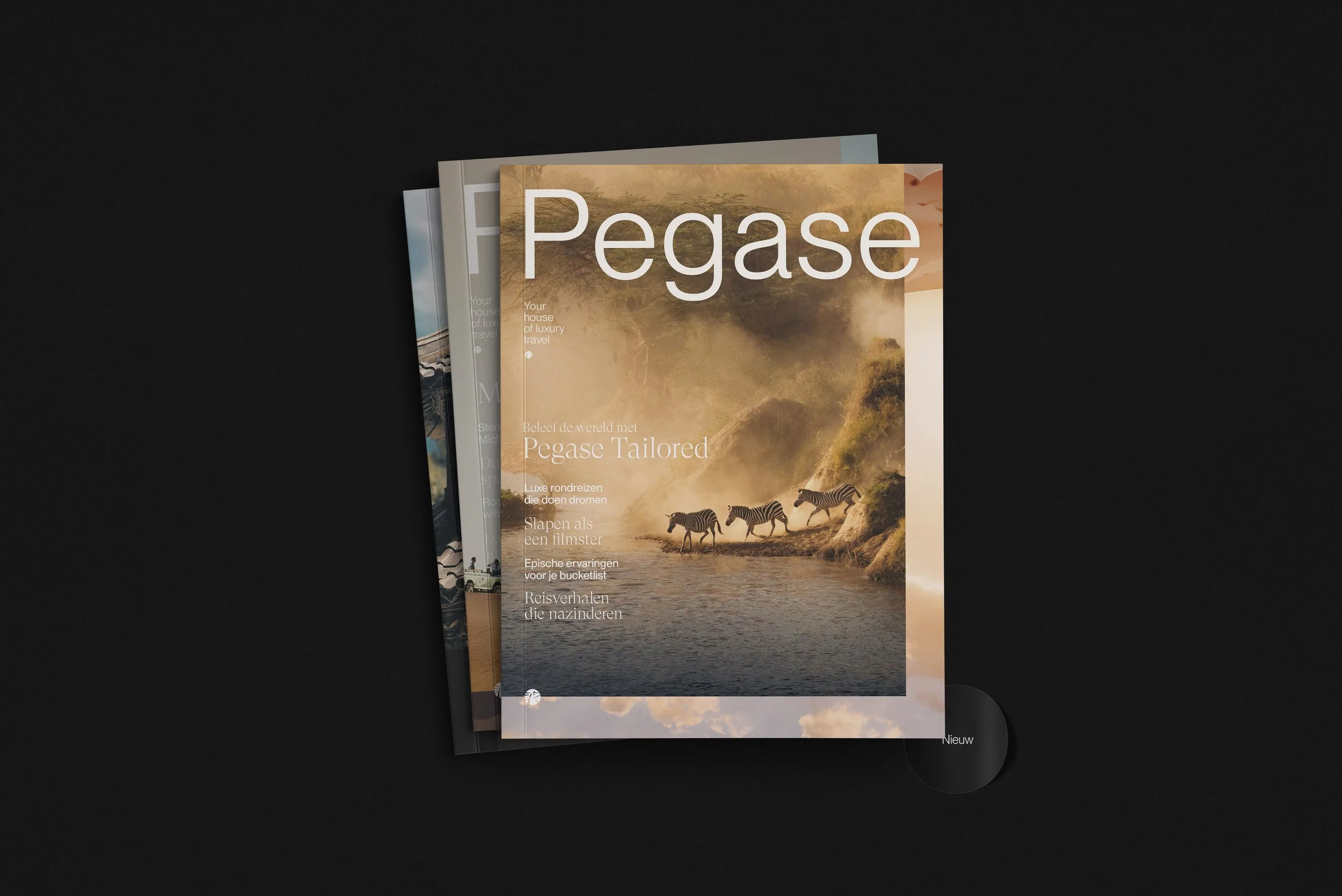 Drie tijdschriften gestapeld op een zwarte achtergrond, de voorste is een magazine met de titel 'Pegase' en een afbeelding van zebra's in een landschap met water en mist.