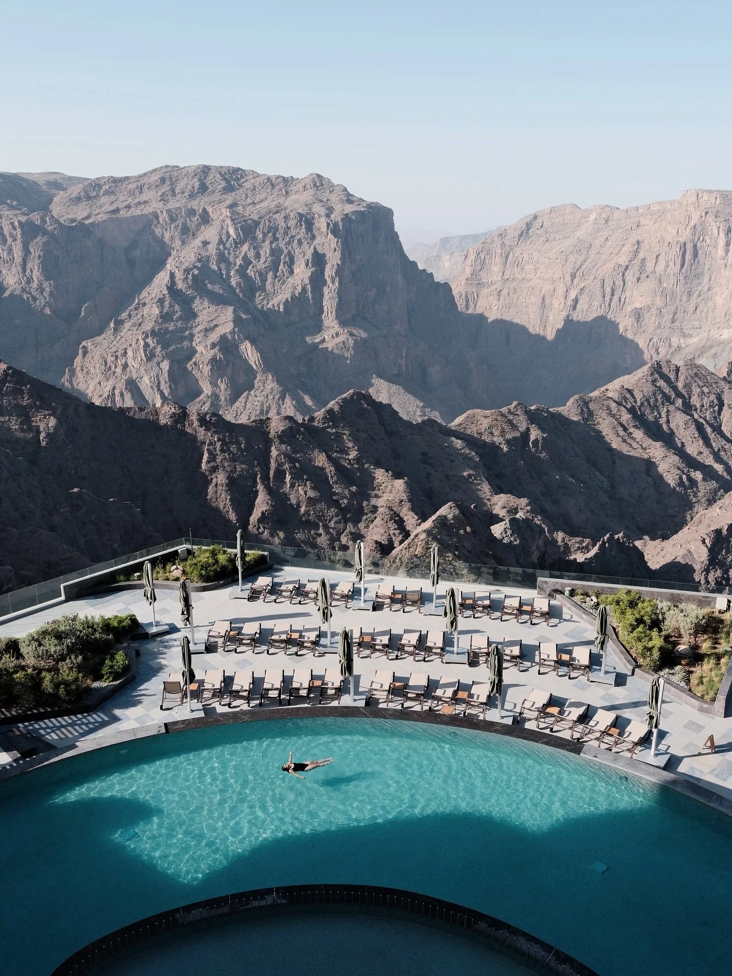Zwemmende persoon in een zwembad met uitzicht op een berglandschap.