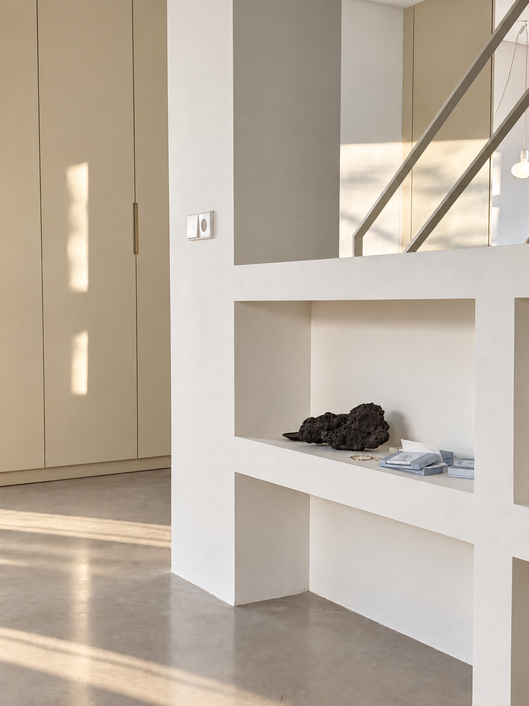 Interieur van een modern huis met witte muren, een deur, een trapleuning en enkele decoratieve objecten op een open nis in de muur.