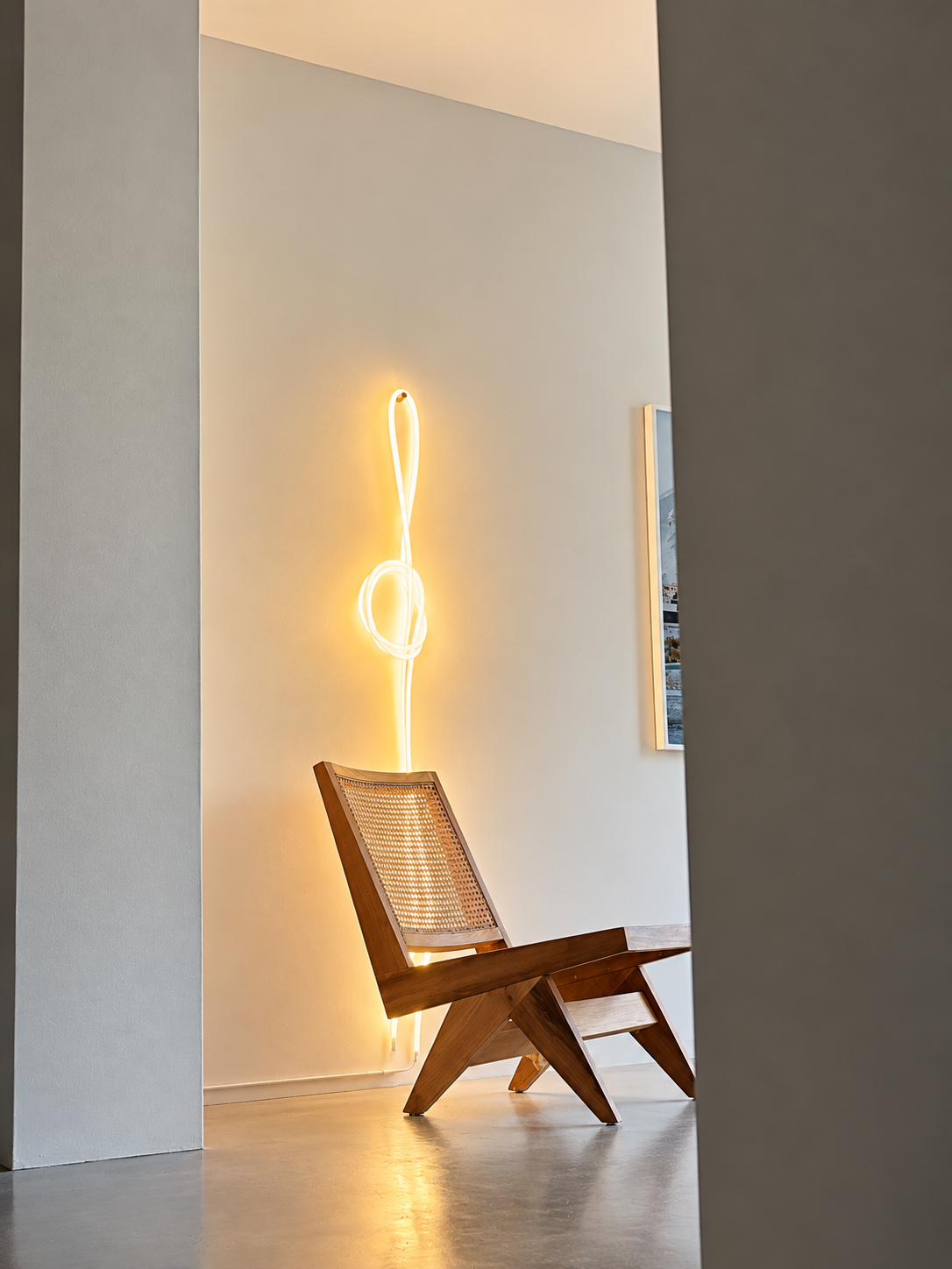 Houten stoel met stalen frame voor een witte muur met een modern lichtkunstwerk in de vorm van een muzieknoot.
