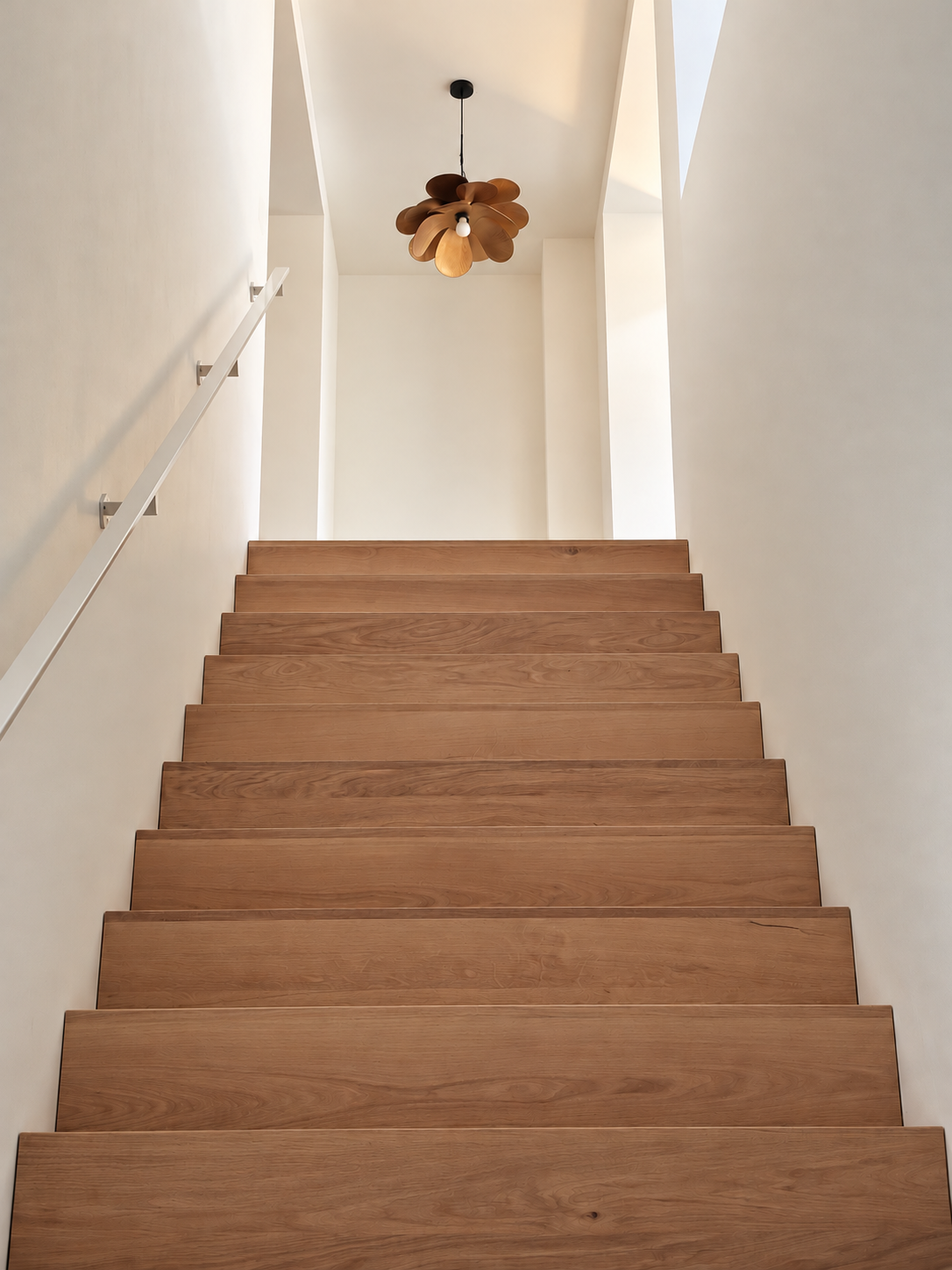 Houten trap met witte muren en een moderne houten plafondlamp.