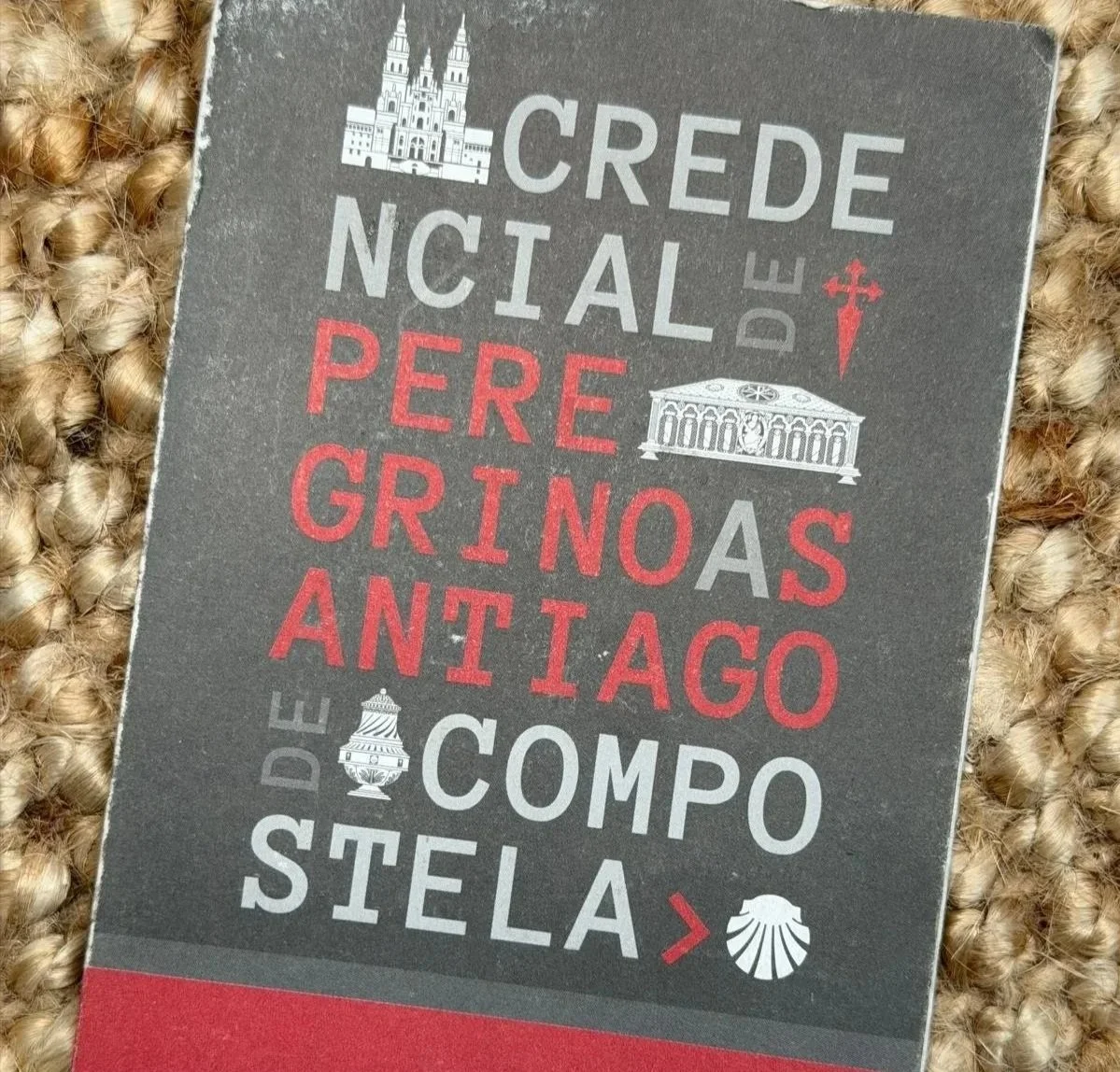 A book titled 'Credencial de Peregrino' with a list of Spanish pilgrimage cities, including Madrid, Compostela, and Santiago, with icons of buildings and shells.
