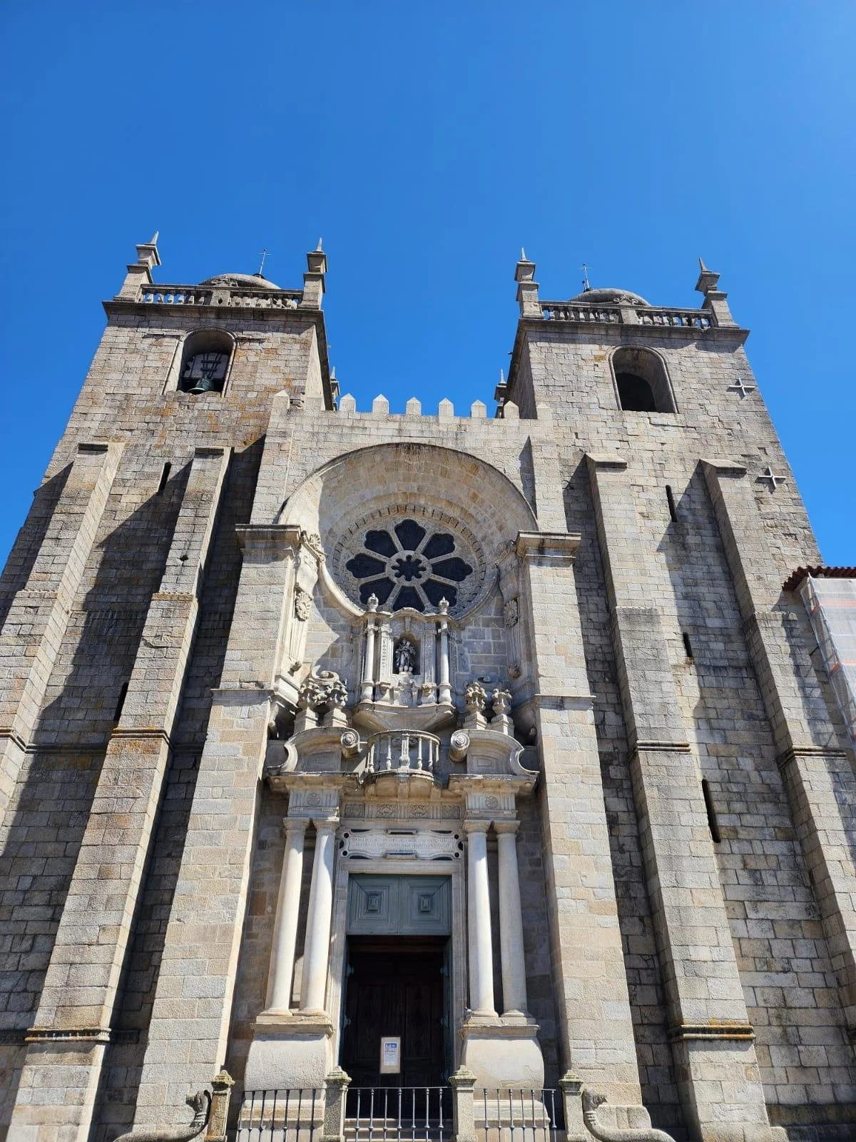 A tall historic stone church with two towers, a large rose window, and ornate architectural details under a bright blue sky.