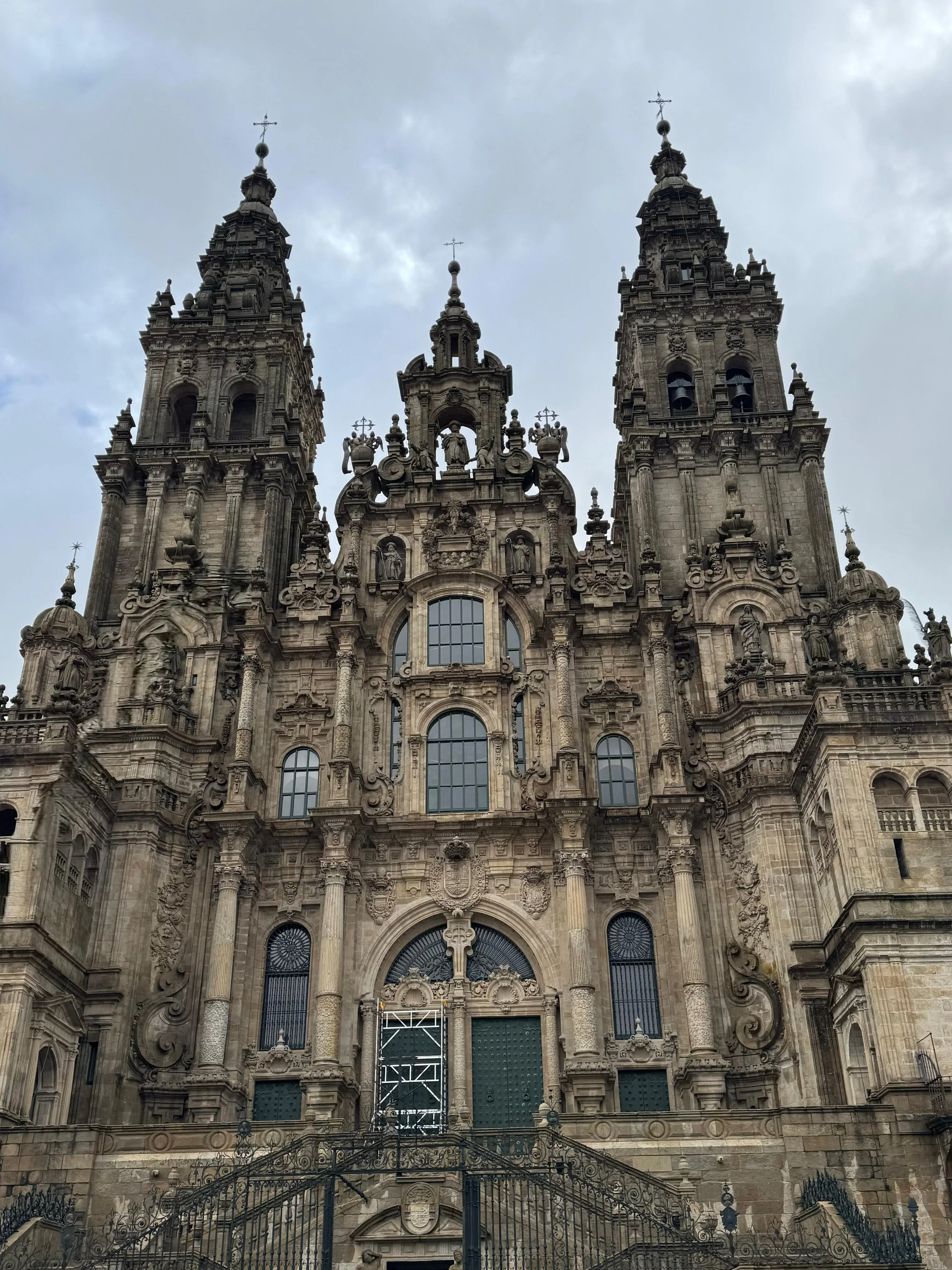 View of a grand, ornate Baroque-style church with twin bell towers and intricate carvings on the facade, with clouds overhead.