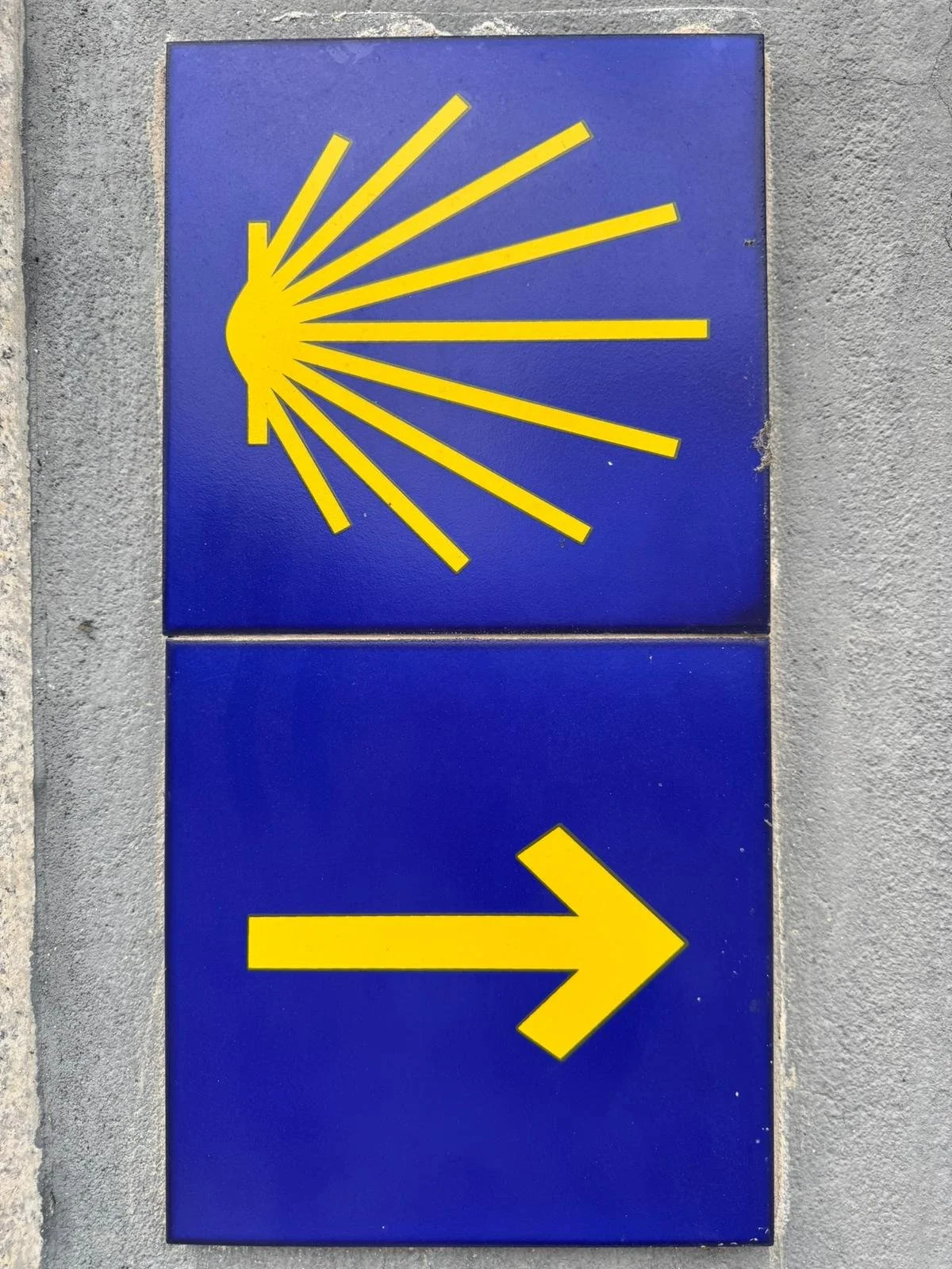 Blue signs with yellow sunburst and arrow symbols indicating directions at a wall. Santiago arrow.