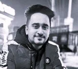 Black and white photo of a man with dark hair and a beard, wearing a jacket, outdoors.