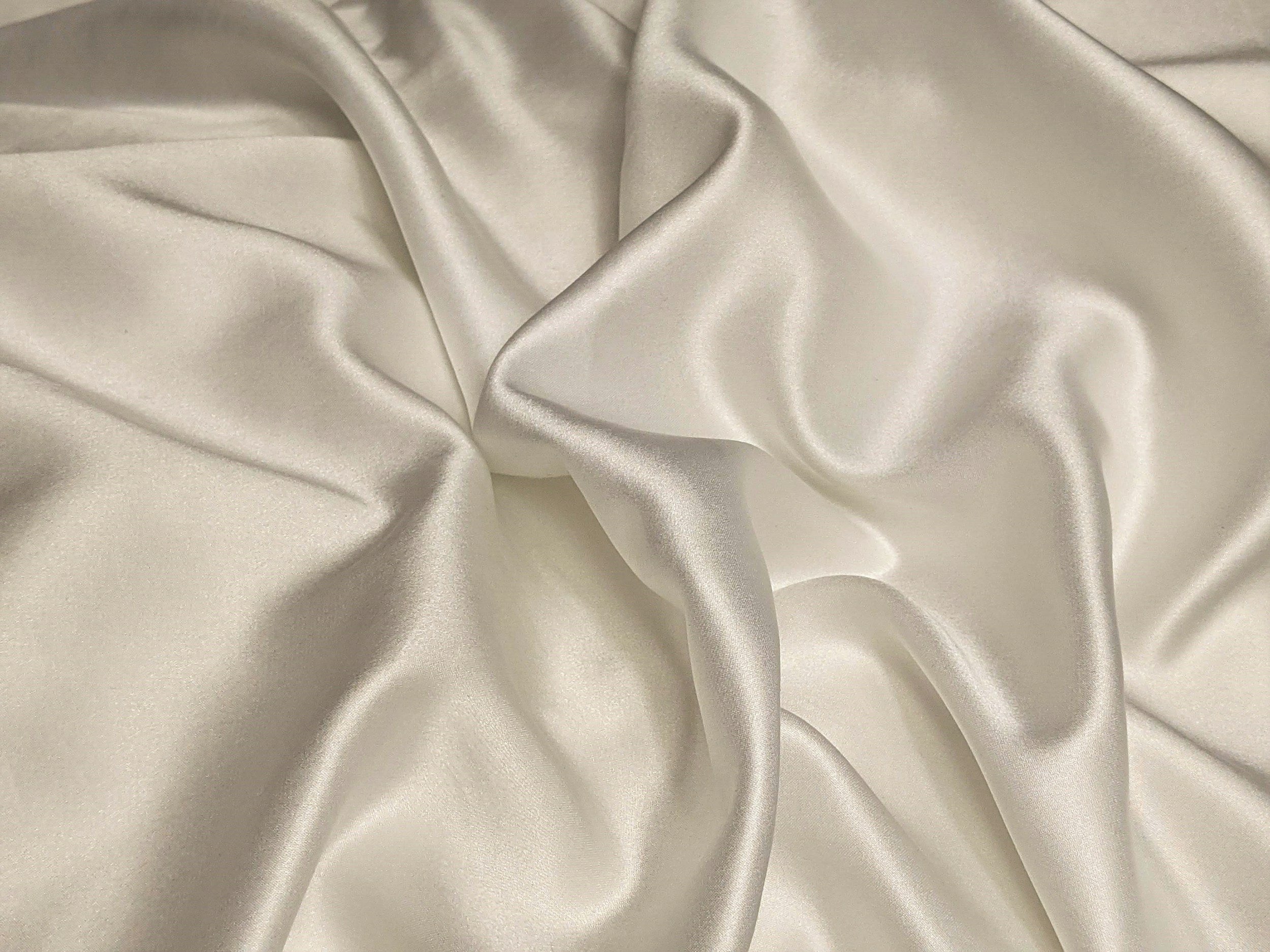Cream-colored silk fabric with a smooth, shiny surface, draped with gentle folds and wrinkles.