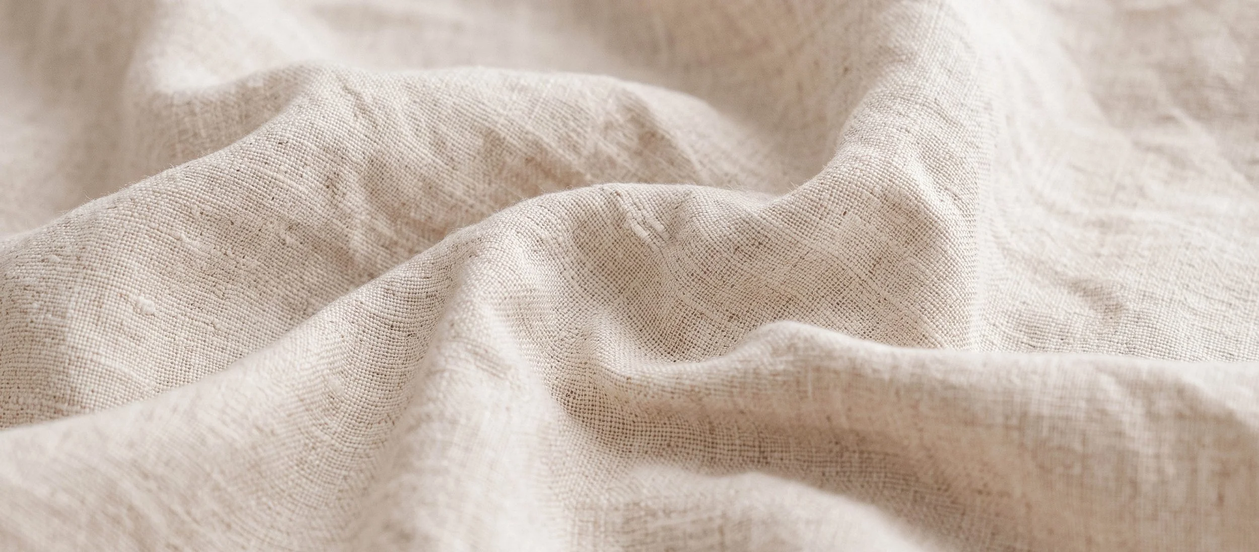 Close-up of beige, textured linen fabric with soft folds.