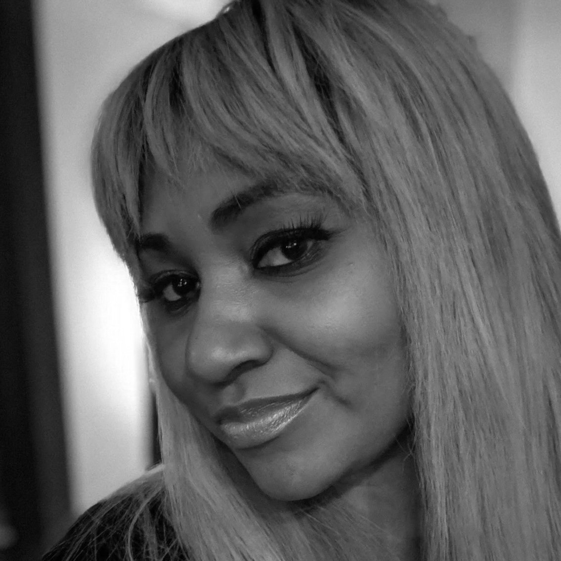 Close-up black-and-white photo of a woman with straight, shoulder-length hair, slightly smiling, looking at the camera.