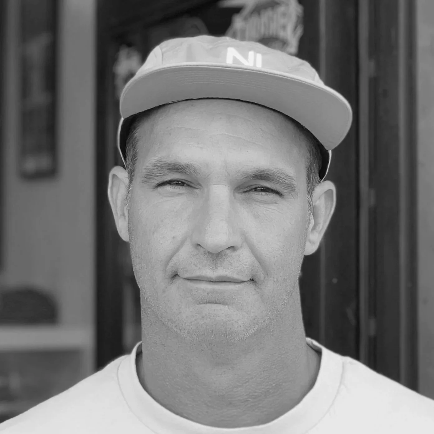 A man wearing a baseball cap with the letters N and I, looking straight at the camera, in black and white.