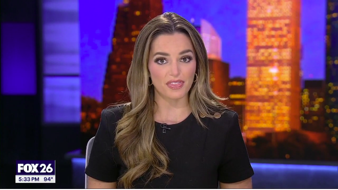 News anchorwoman on FOX 26 presenting in front of a city skyline backdrop during evening news.