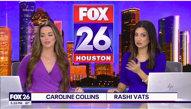 Two female news anchors sit at a desk with a FOX 26 Houston background behind them. The anchor on the left, Caroline Collins, has long brown hair and wears a purple top. The anchor on the right, Rashi Vats, has long dark hair and wears a blue top. There are laptops in front of them, and a city skyline is visible in the background.
