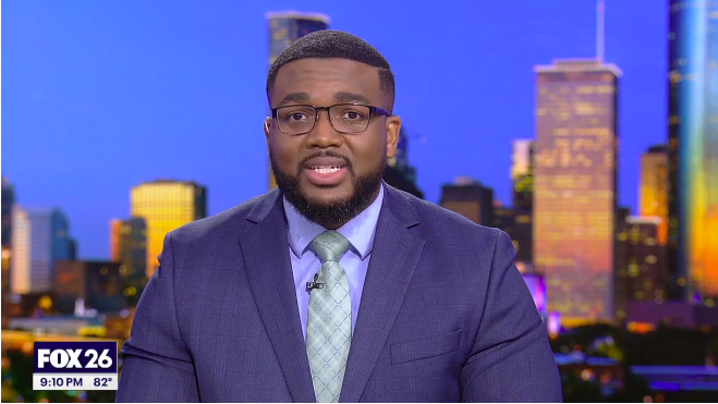 Television news anchor reporting for FOX 26 with city skyline background at night