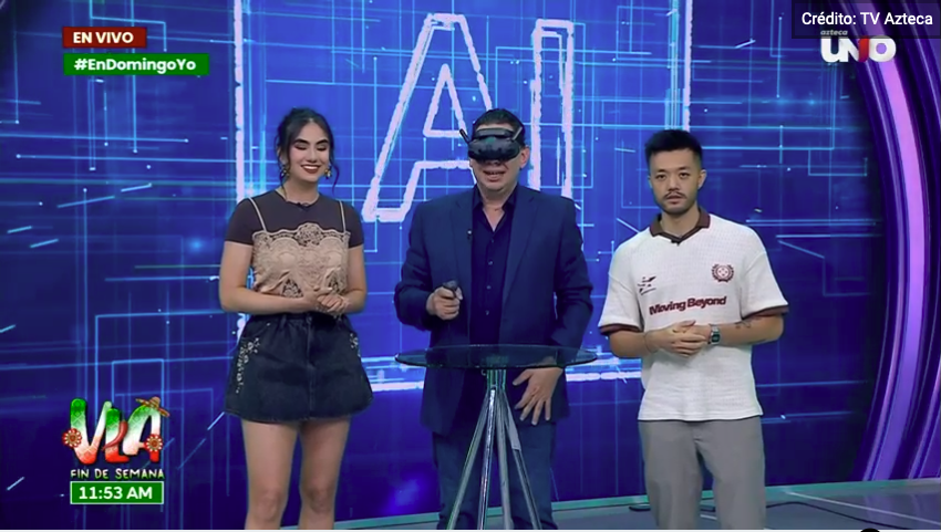 Three TV show hosts on a blue digital-themed set, with one man wearing a virtual reality headset, a woman in a black and beige dress, and another man in a white sports jersey.