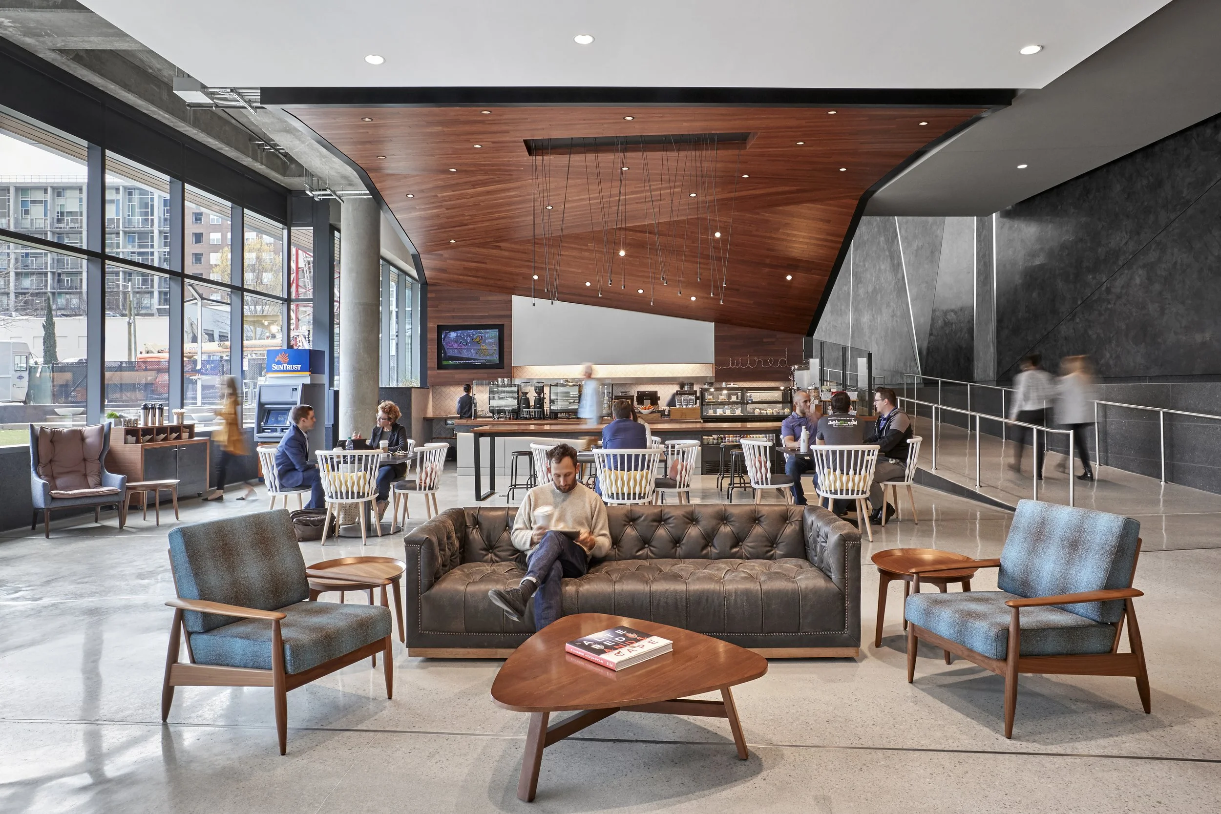 Modern coffee shop with seating area, window wall, and staircase to the right, people sitting and walking.