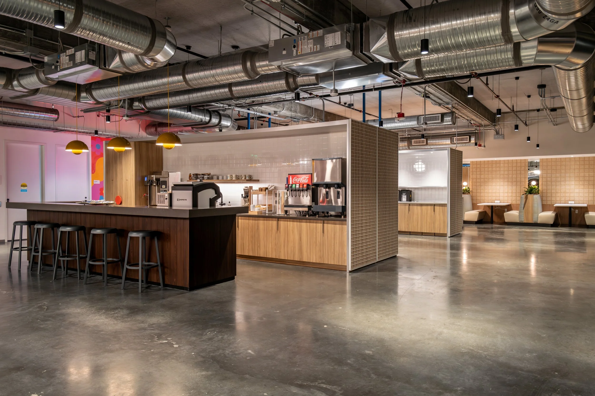 Modern, empty cafe interior with a coffee bar, seating area with tables and chairs, exposed ductwork, and contemporary decor.