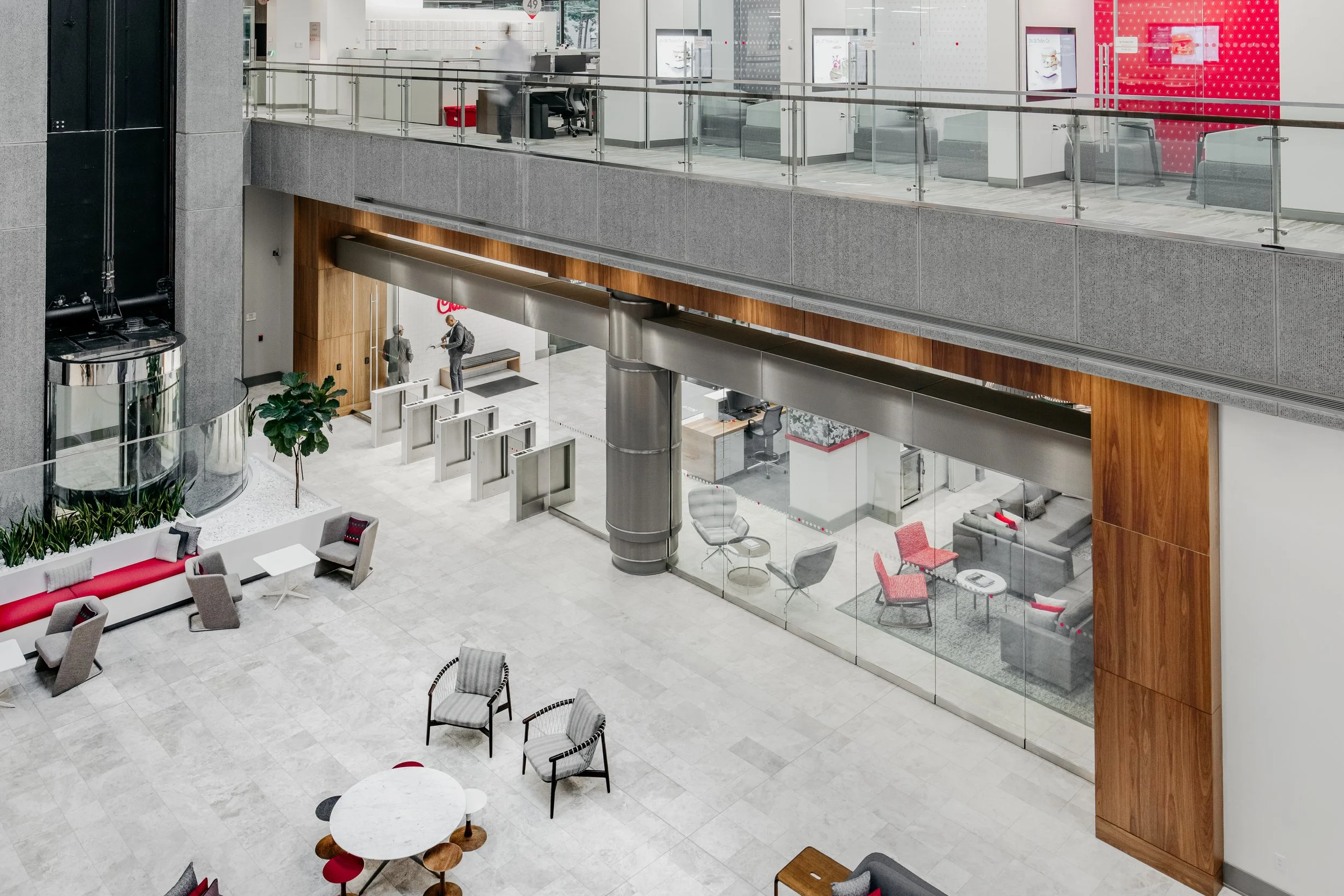 Interior of a modern office building lobby with seating area, plants, and glass enclosed meeting rooms.